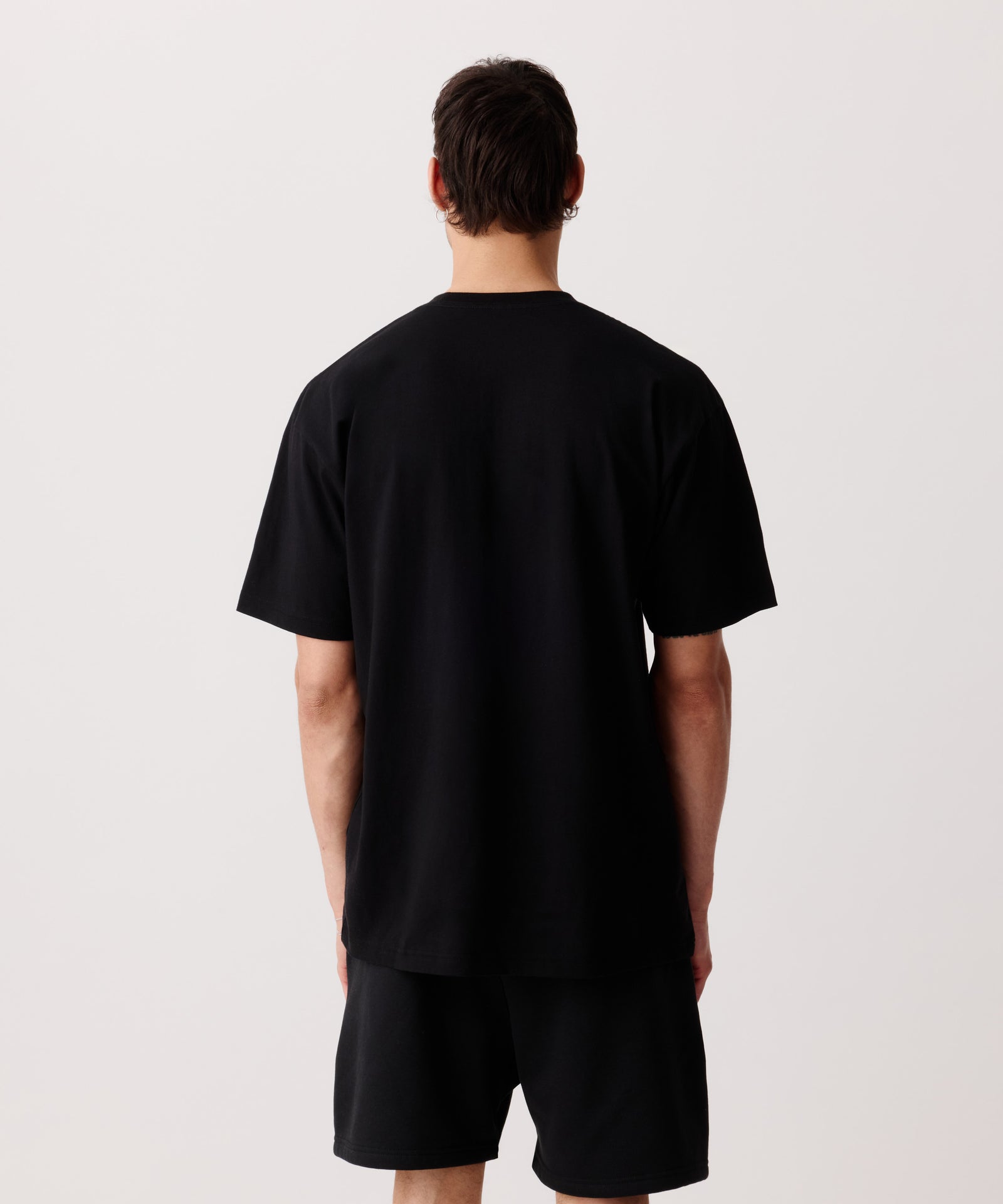 Das Bild zeigt das schwarze Basic T-Shirt getragen von einem Mann von hinten. Er trägt dazu eine schwarze Shorts.