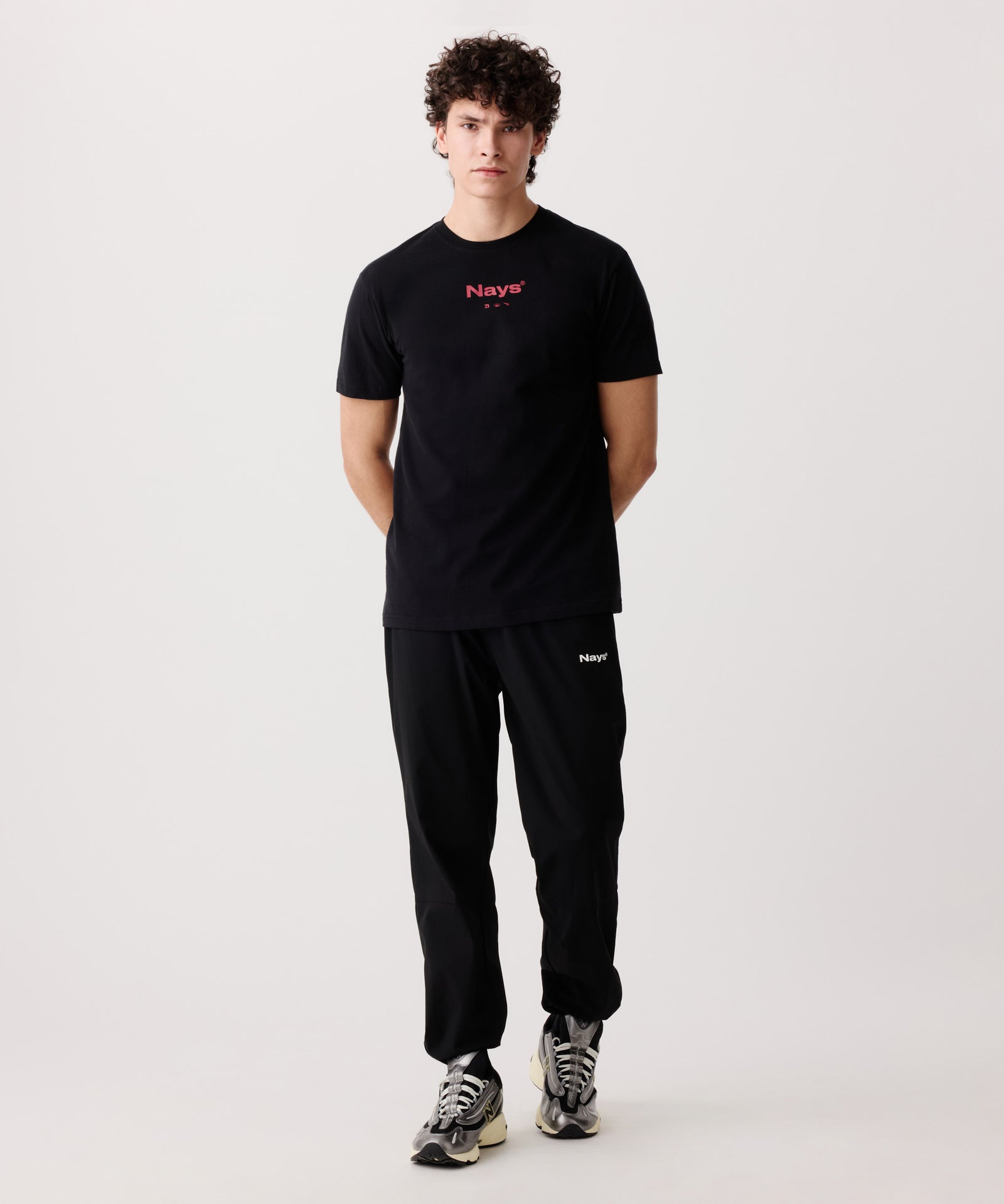 Das Pro Tackle T-Shirt getragen von einem Mann. Seine Arme sind hinter dem Rücken verschränkt und er trägt eine lange, schwarze Hose, sowie helle Turnschuhe.