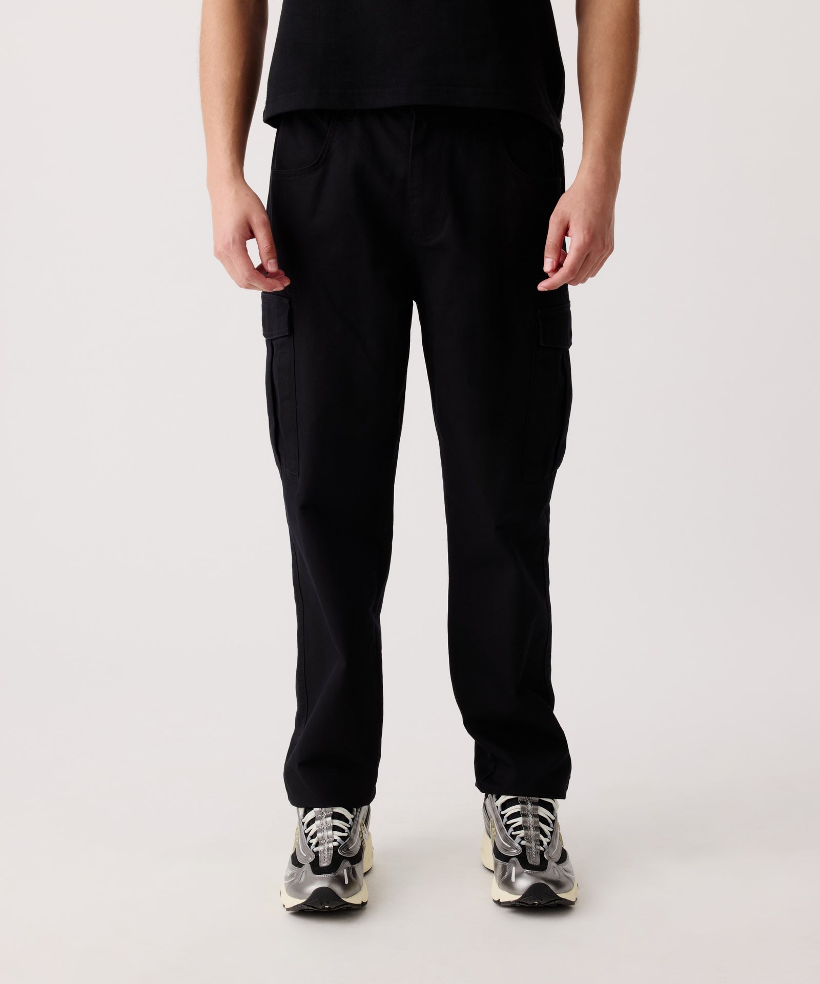 Das Detail-Bild zeigt die Nays Hose aus Baumwolle getragen von einem Mann. Er trägt ein schwarzes T-Shirt und helle Turnschuhe dazu.