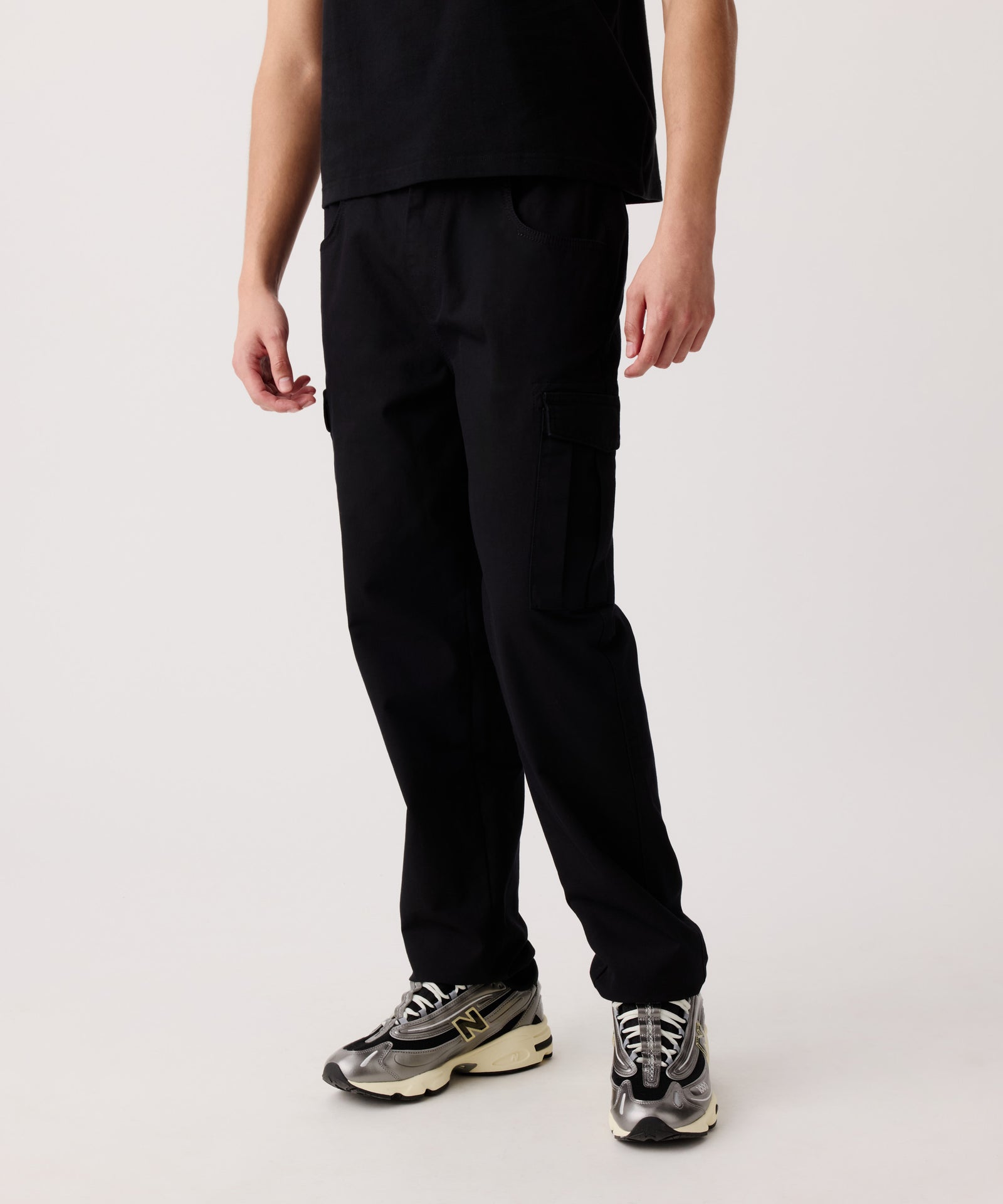 Das Detail-Bild zeigt die Nays Hose aus Baumwolle getragen von einem Mann. Er trägt ein schwarzes T-Shirt und helle Turnschuhe dazu.