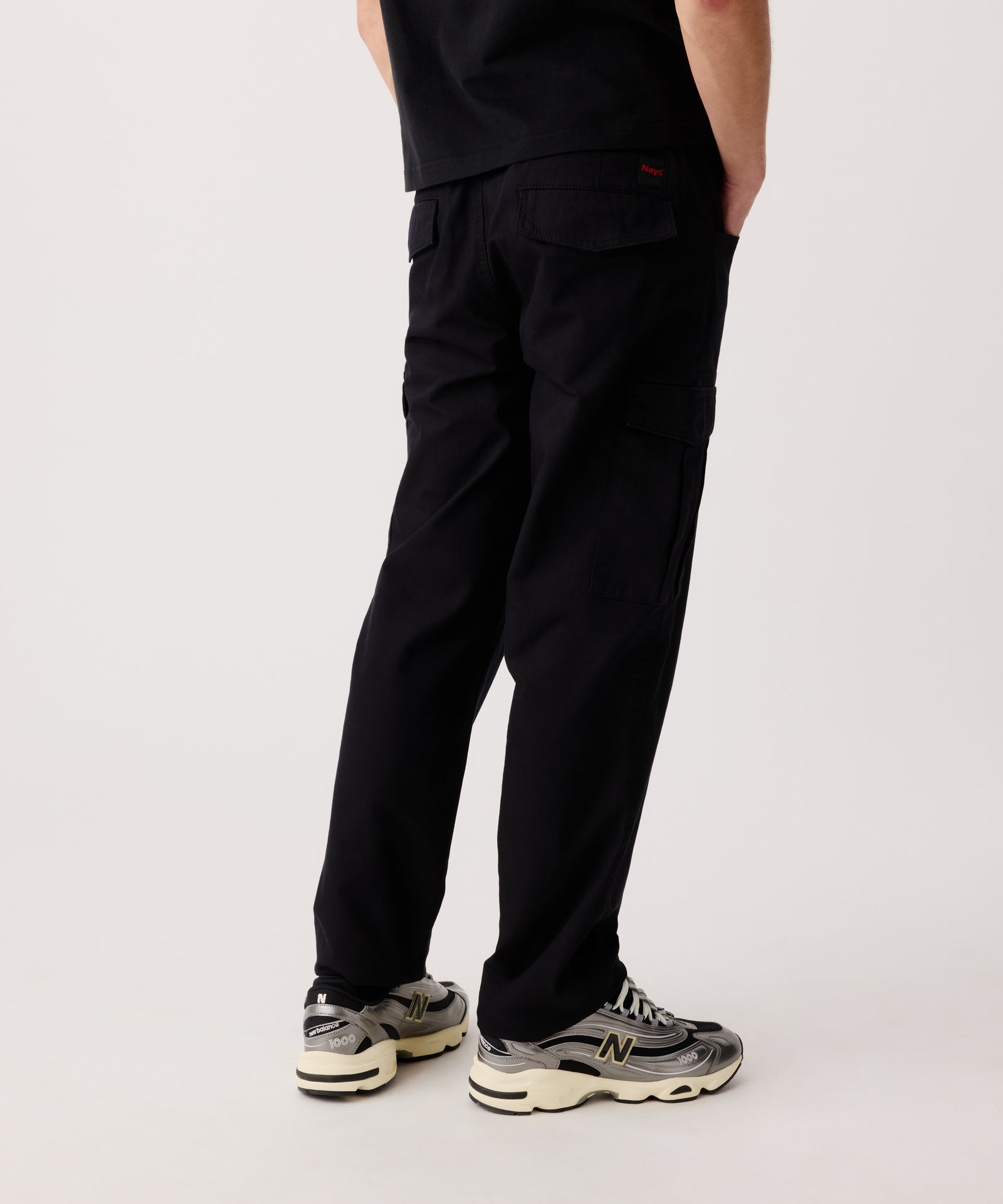 Das Detail-Bild zeigt die Nays Hose aus Baumwolle getragen von einem Mann in der Rückansicht. Er trägt ein schwarzes T-Shirt und helle Turnschuhe dazu.