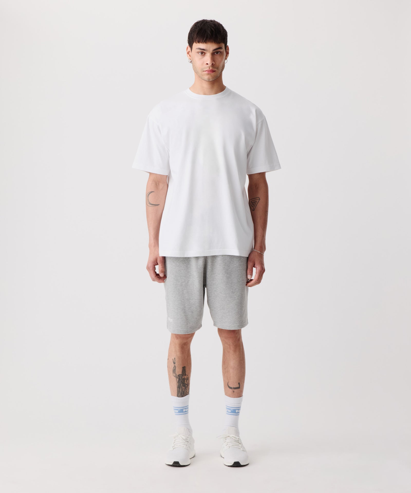 Das Bild zeigt die Nays Shorts in grau getragen von einem Mann. Er trägt ein weißes T-Shirt, weiße Logo Socken und helle Turnschuhe.