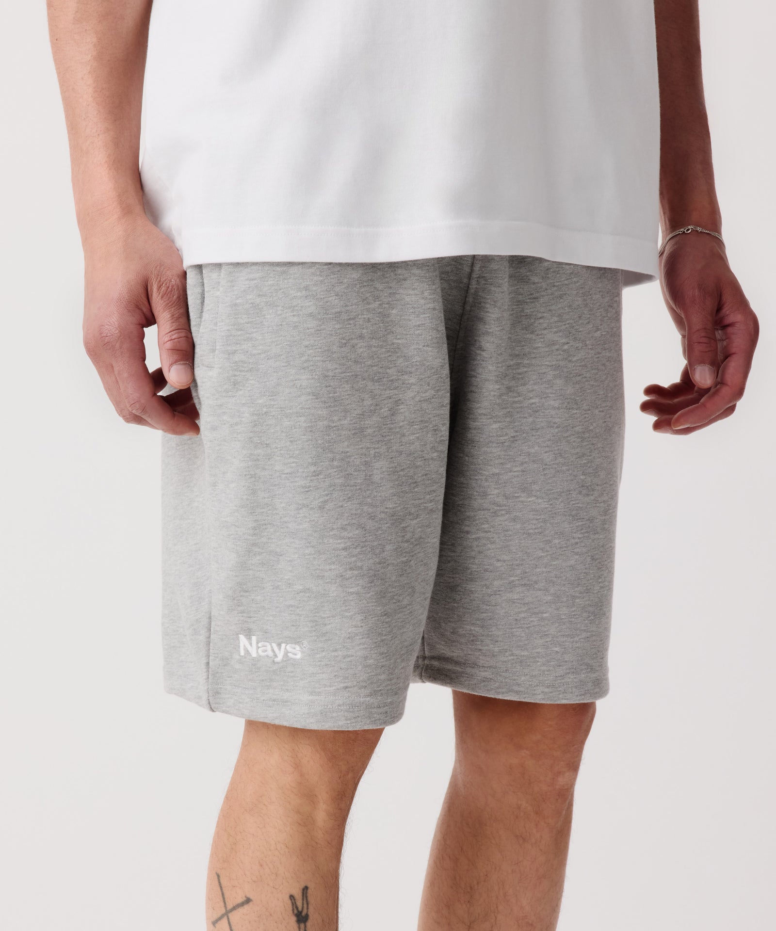 Das Bild zeigt im Fokus die Nays Shorts in grau getragen von einem Mann. Er trägt ein weißes T-Shirt dazu.