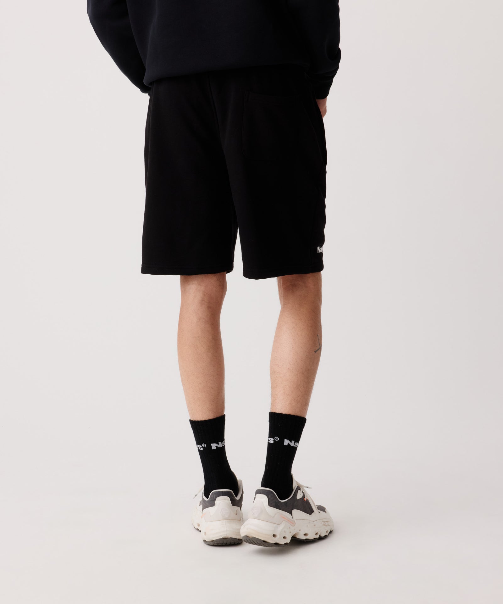 Der Bildausschnitt zeigt die Nays Shorts in schwarz getragen von einem Mann in der Rückansicht. Dazu trägt er schwarze Socken und helle Turnschuhe.