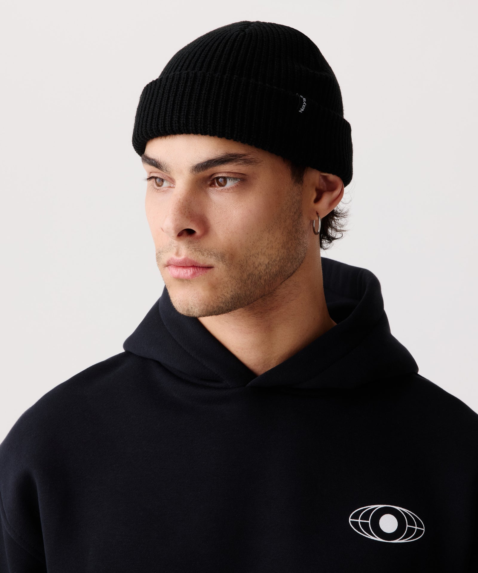 Schwarze Strickmütze mit gerippter Textur getragen von einem Mann im Halbseiten-Profil. Kombiniert mit einem schwarzen Kapuzen-Pullover.