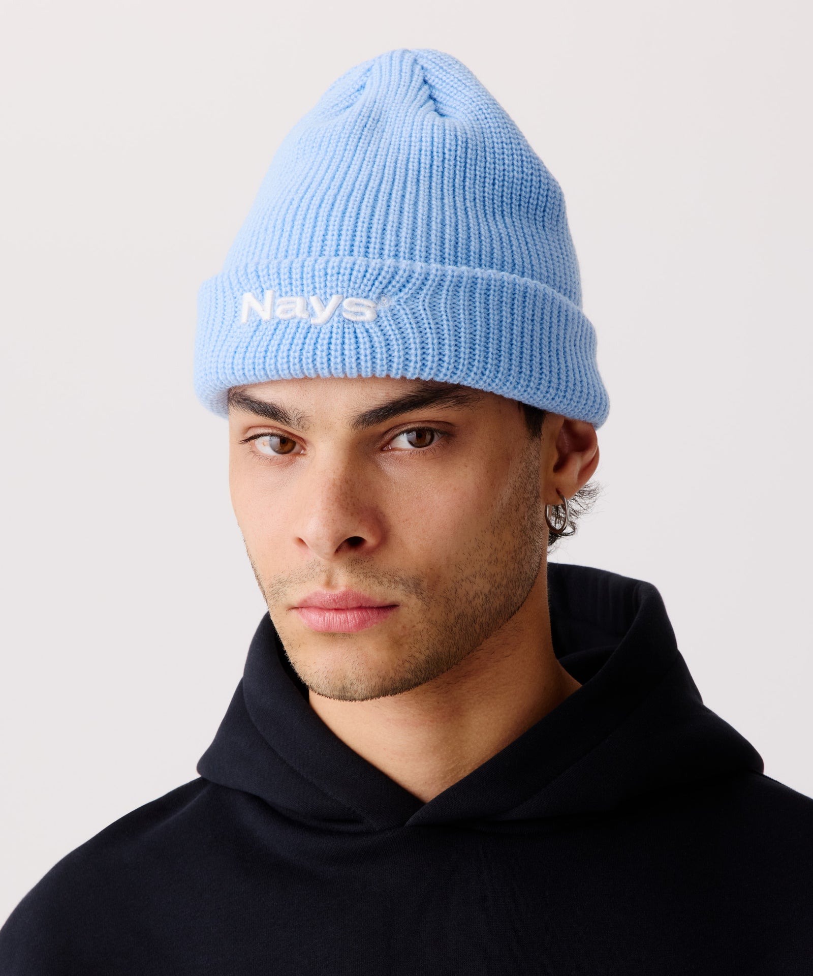 Auf dem Bild ist eine hell-blaue Strickmütze zu sehen getragen von einem Mann. Er trägt dazu einen schwarzen Pullover mit Kapuze.