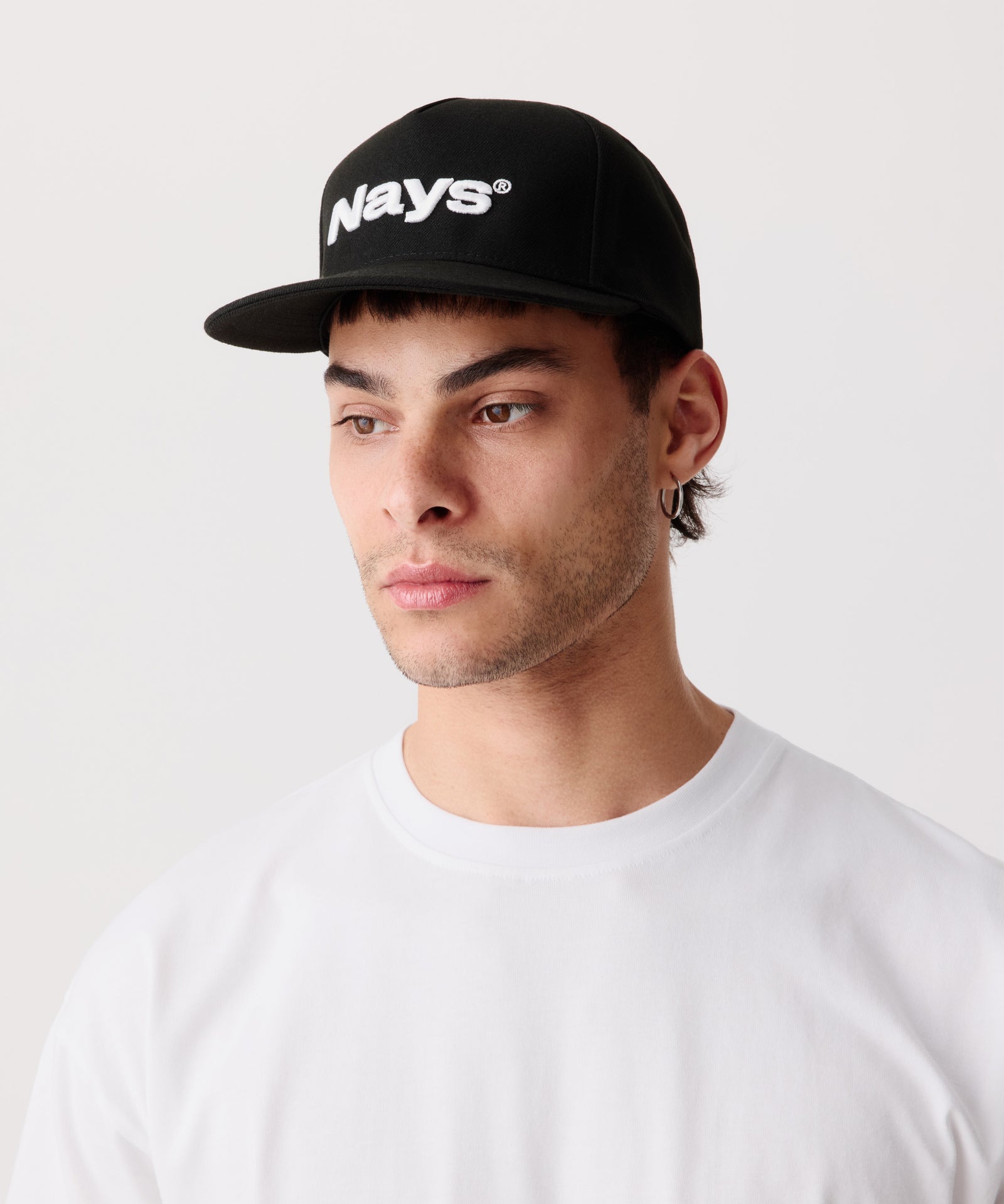 Das Bild zeigt eine schwarze Schirm-Mütze mit einem weißem Logo getragen von einem Mann in der Seiten-Perspektive. Er trägt dazu ein weißes T-Shirt.