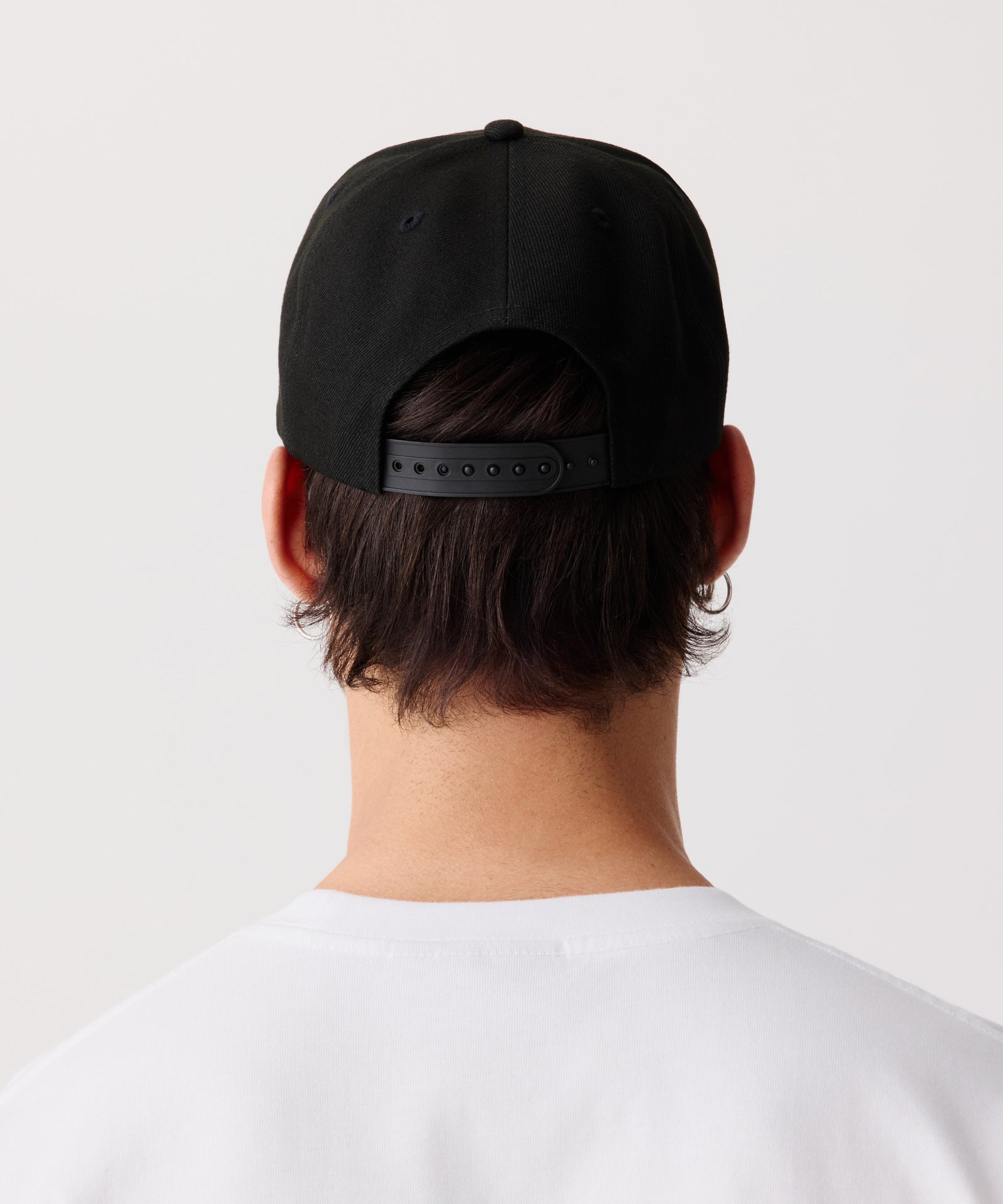 Das Bild zeigt eine schwarze Schirm-Mütze mit einem weißem Logo getragen von einem Mann in der Rückansicht.