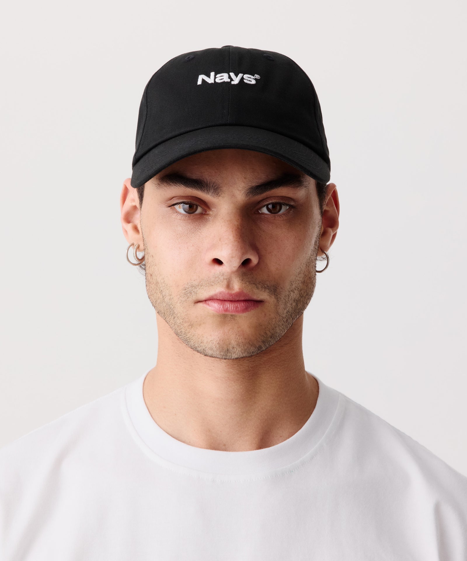 Eine sportliche Schirm-Mütze mit mittig gesticktem Nays Logo. Das Model trägt dazu ein weißes T-Shirt.