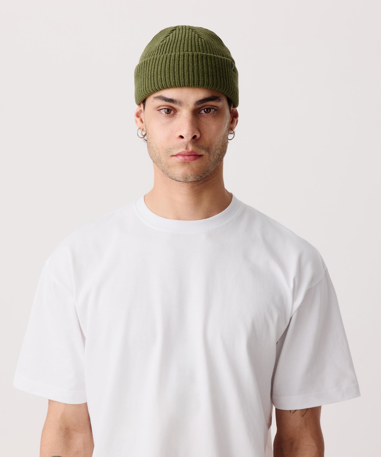 Oliv-Grüne Strickmütze mit gerippter Textur getragen von einem Mann. Dazu trägt er ein weißes T-Shirt.