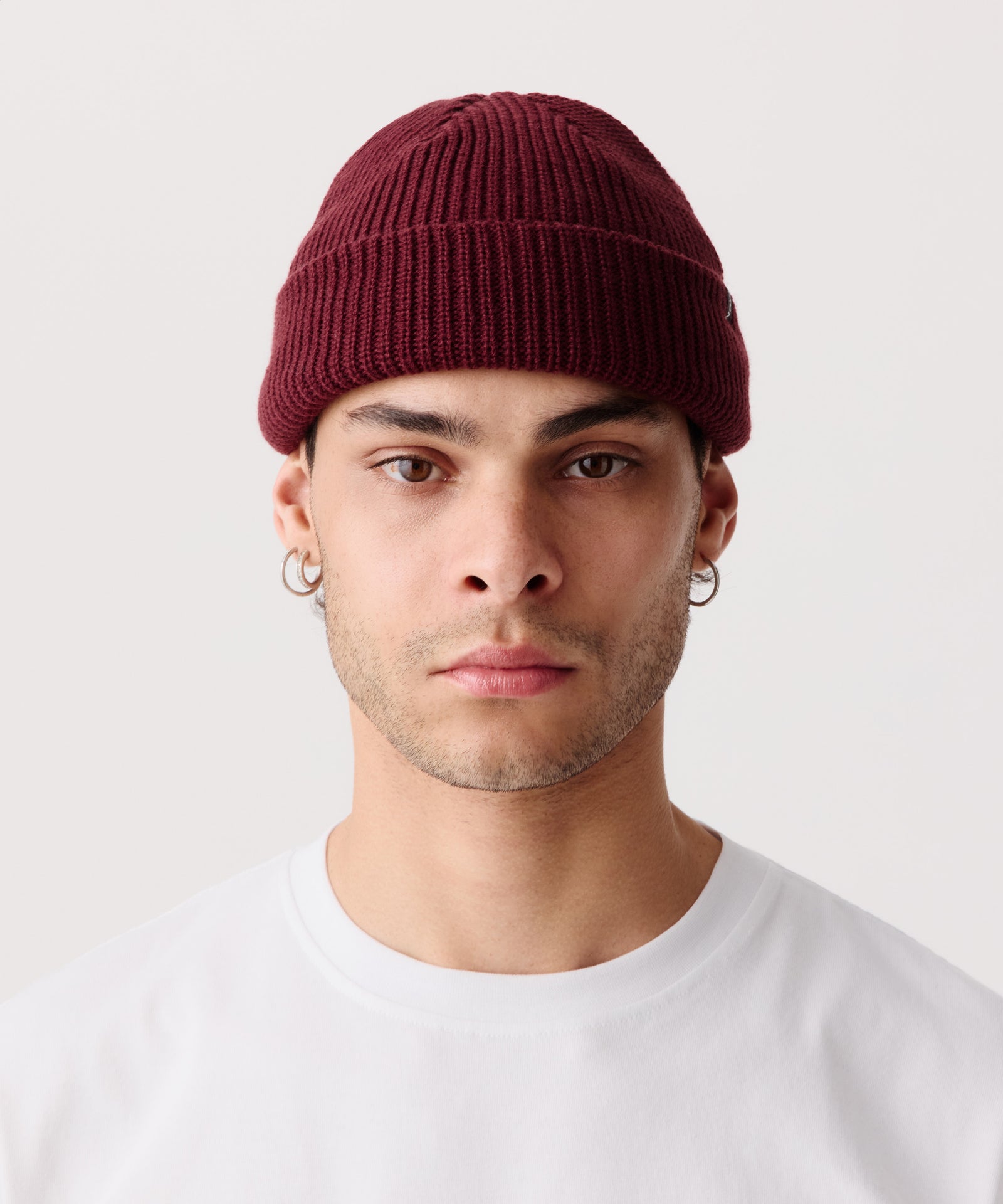 Weinrote Strickmütze mit gerippter Textur getragen von einem Mann. Dazu trägt er ein weißes T-Shirt.