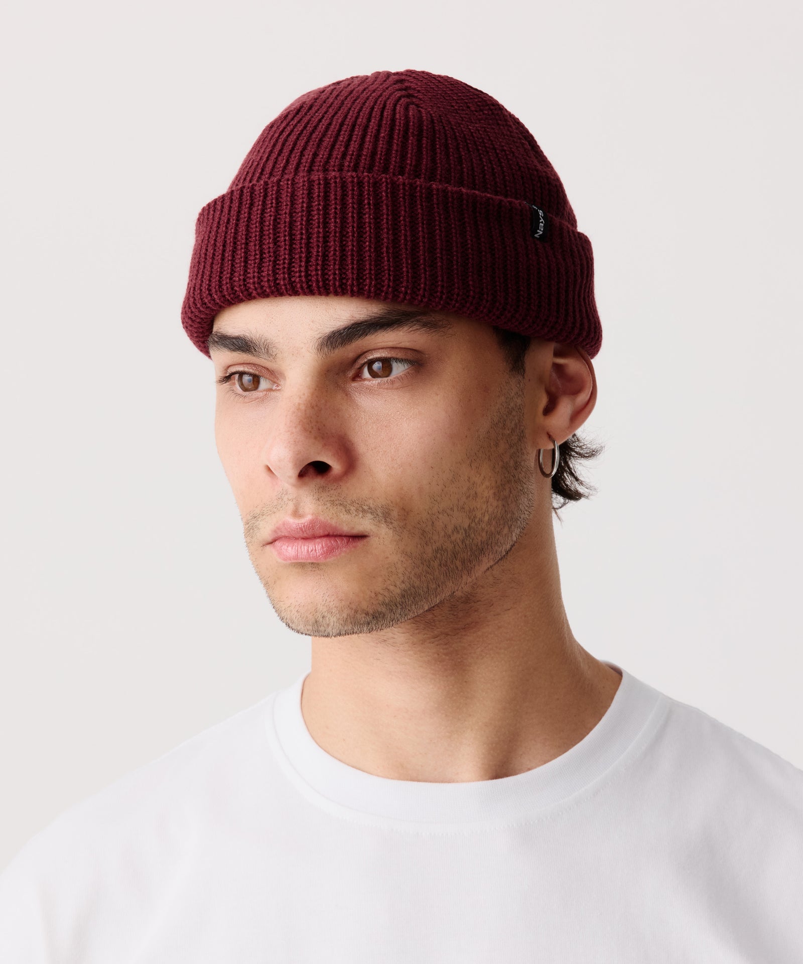 Weinrote Strickmütze mit gerippter Textur getragen von einem Mann im Halbseiten-Profil. Dazu trägt er ein weißes T-Shirt.