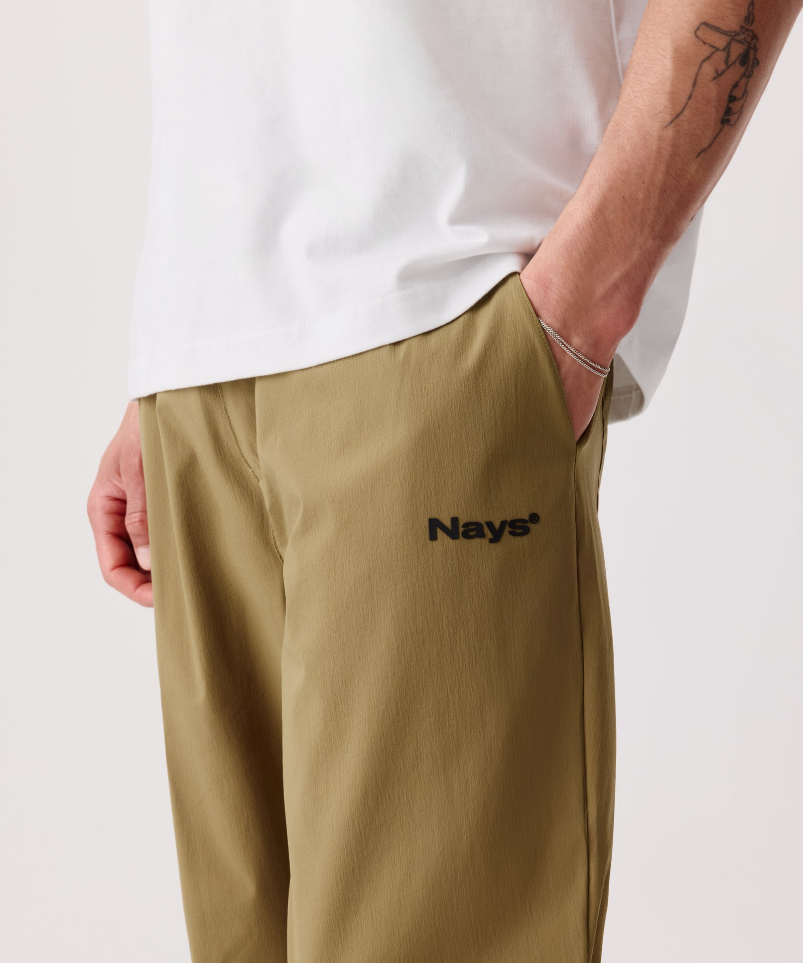 Das Detail-Bild zeigt die Nays Summer Pants. Eine Hand steckt in der Hosentasche, der Fokus liegt auf dem schwarzen Logo.