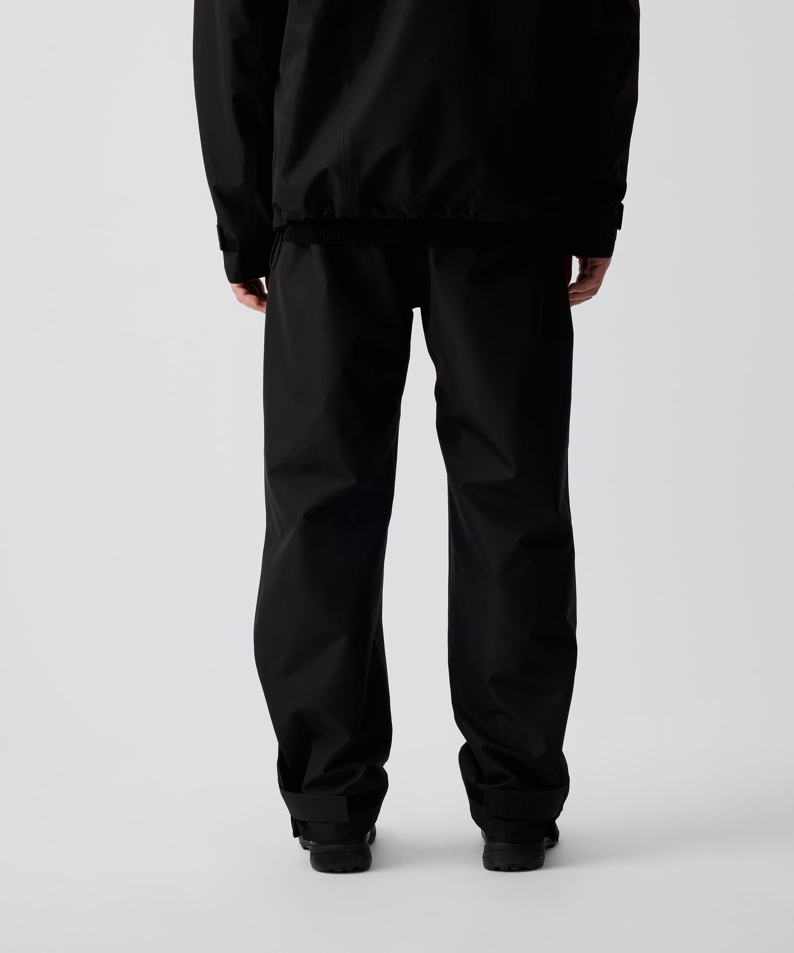 Nays 3L Multifunctional Rain Pants in der Rückansicht getragen von einer Person, zeigt ergonomische Passform und Reißverschlüsse am Beinsaum für einfaches An- und Ausziehen über Schuhe.