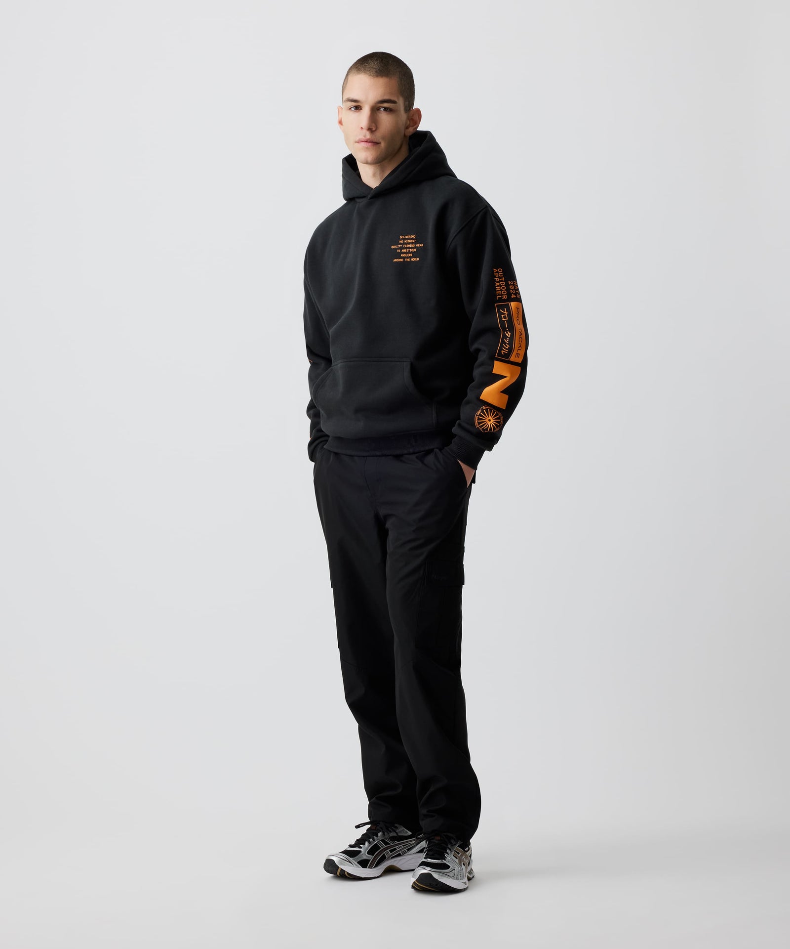 Mann trägt Nays Quote Hoodie mit auffälligem orangefarbenem Nays-Print im Halbseiten Profil. Schwarzer Hoodie aus Baumwoll-Polyester-Mix, ideal für den Alltag und kühleres Wetter.