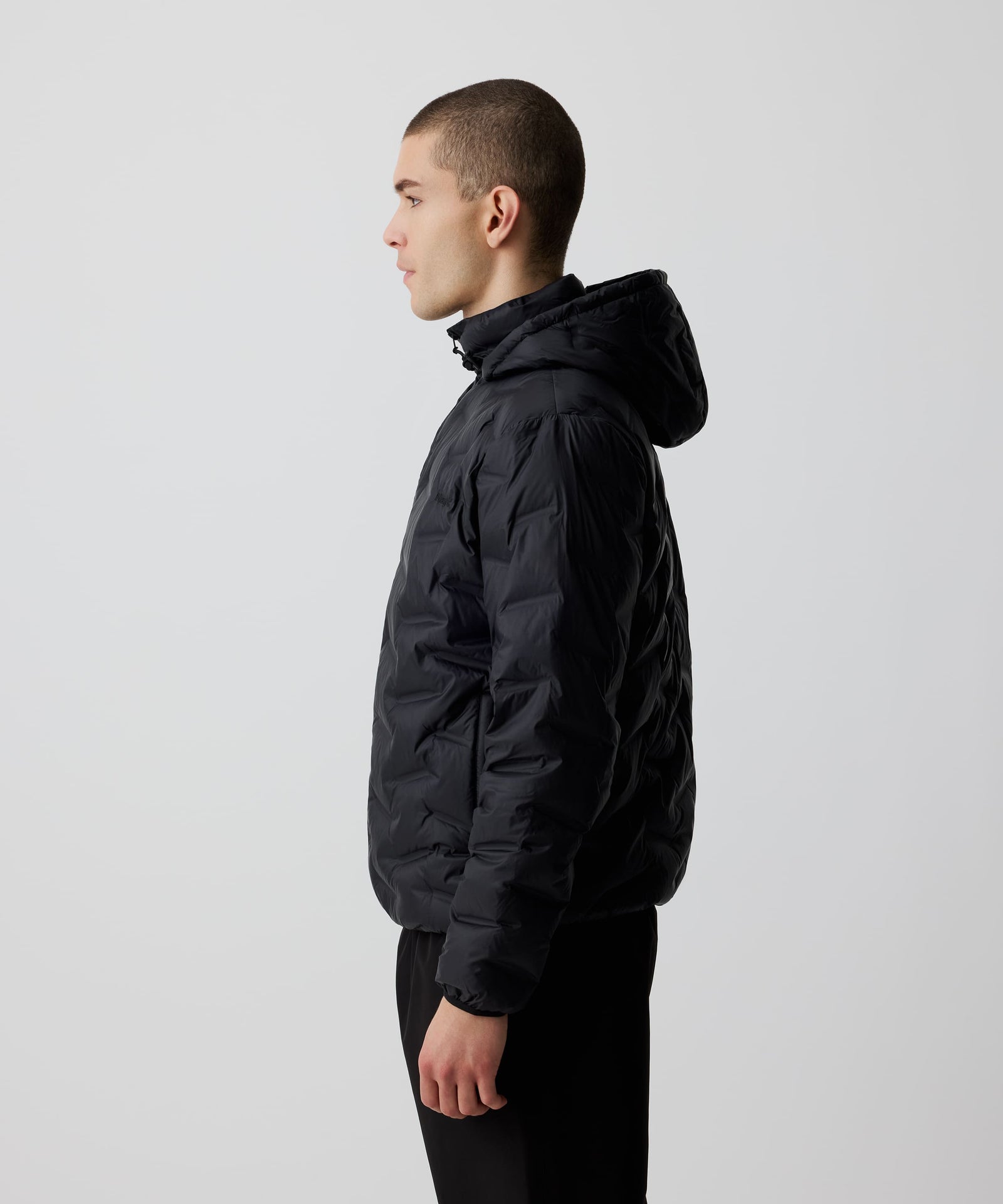 Ein Mann trägt die Nays Lightweight Down Jacket mit Kapuze in der Seitenansicht, Reißverschlüssen und Seitentaschen, ideal für kalte Tage und Outdoor-Abenteuer.