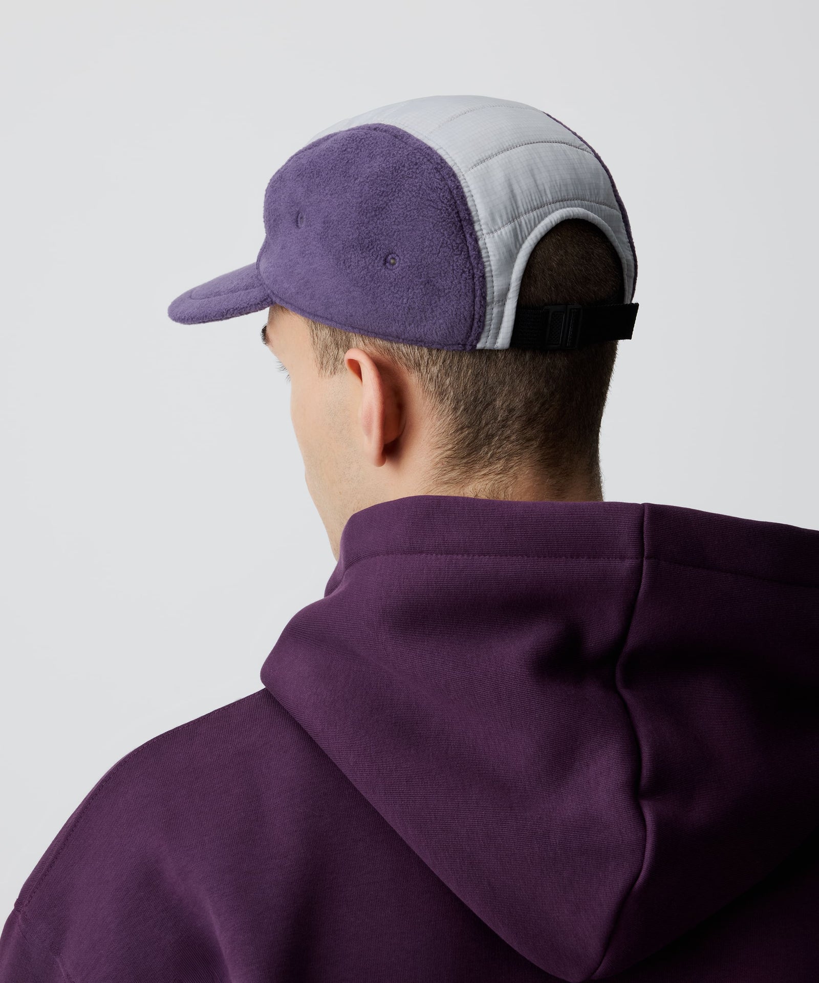 Nays Sherpa 5 Panel Cap aus weichem flieder-farbigem Sherpa-Material und gefüttertem, weiß abgesetzten Ripstop am Kopf getragen von einem Mann in der Rückansicht.