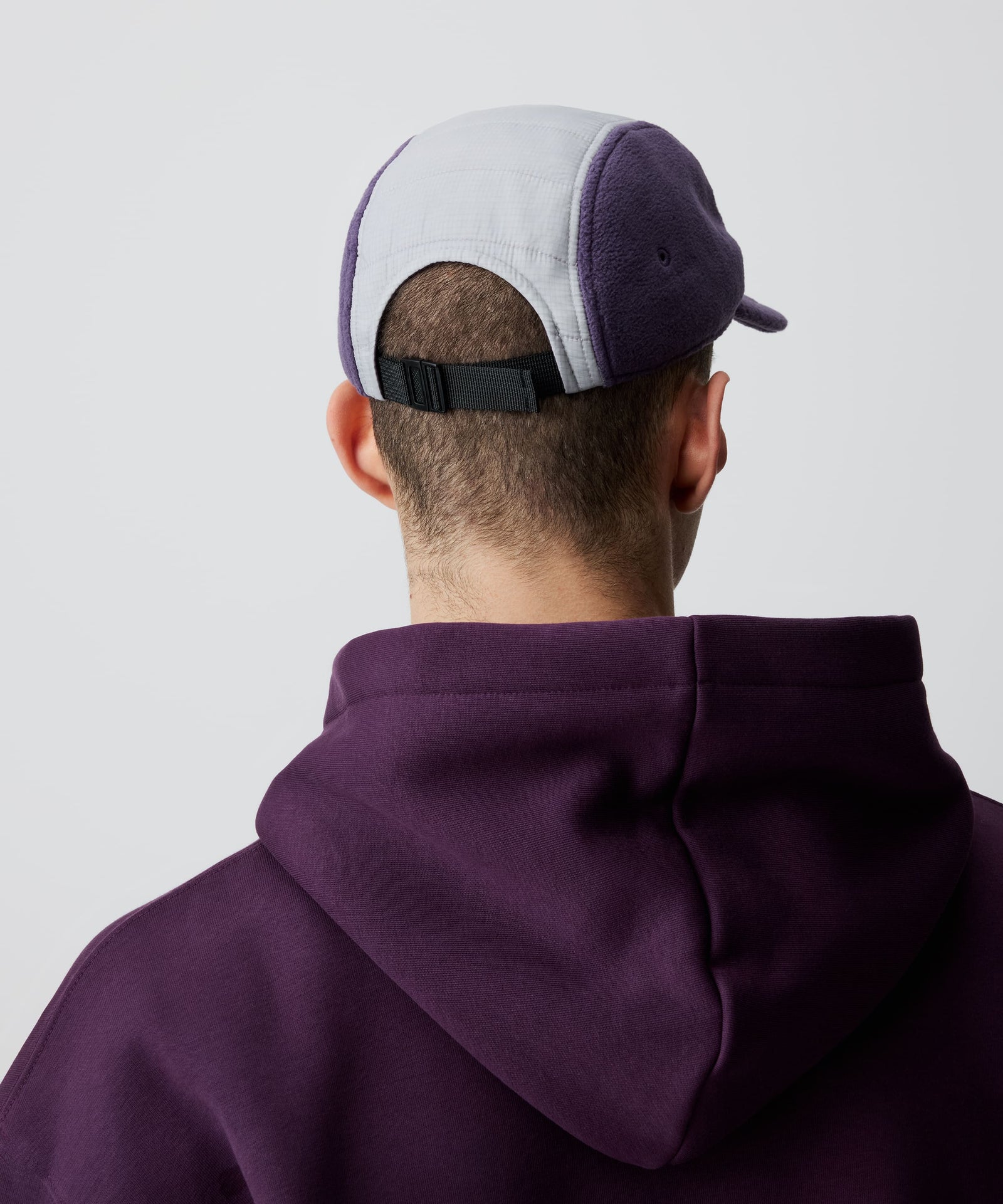 Nays Sherpa 5 Panel Cap aus weichem flieder-farbigem Sherpa-Material und gefüttertem, weiß abgesetzten Ripstop am Kopf getragen von einem Mann in der Rückansicht.