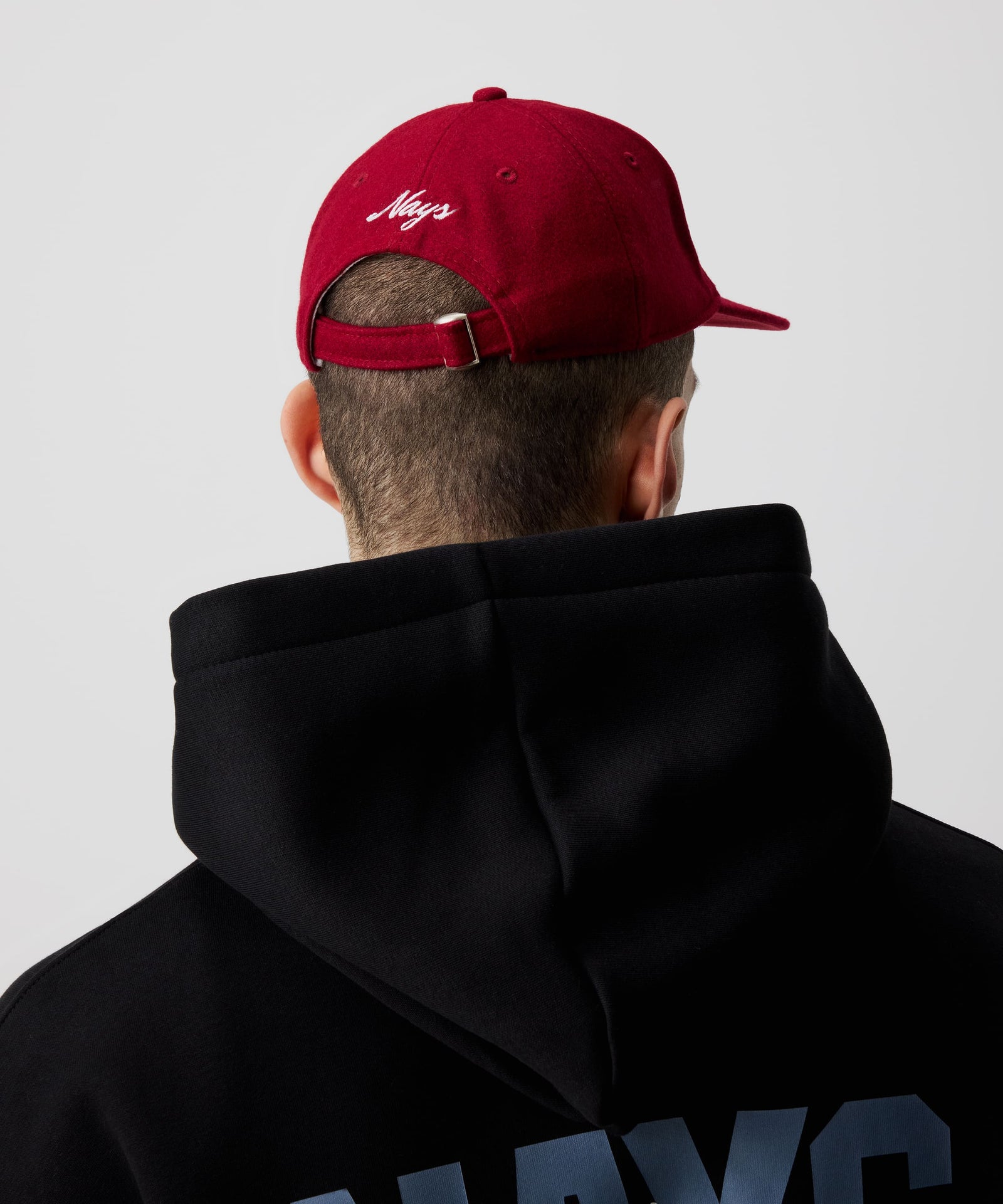 Mann trägt rote Nays Felt Cap, eine Schirmmütze aus Filz kombiniert mit einem schwarzen Kapuzen-Pullover in der Rückansicht.