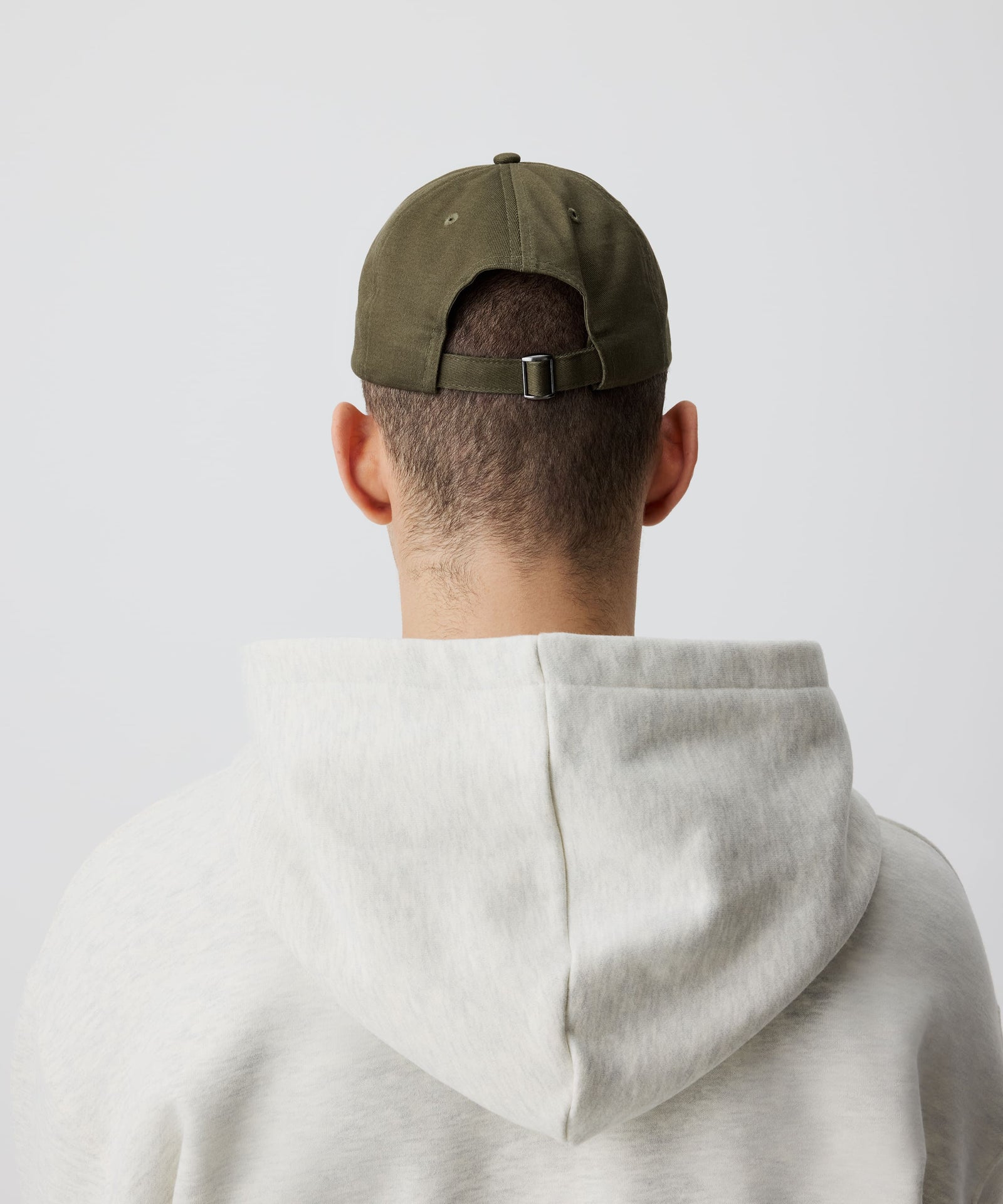 Ein weiteres Detail-Bild unserer khaki-farbenen Schirm-Mütze getragen von einem Mann von hinten. Dazu trägt er einen grauen Kapuzen-Pullover.