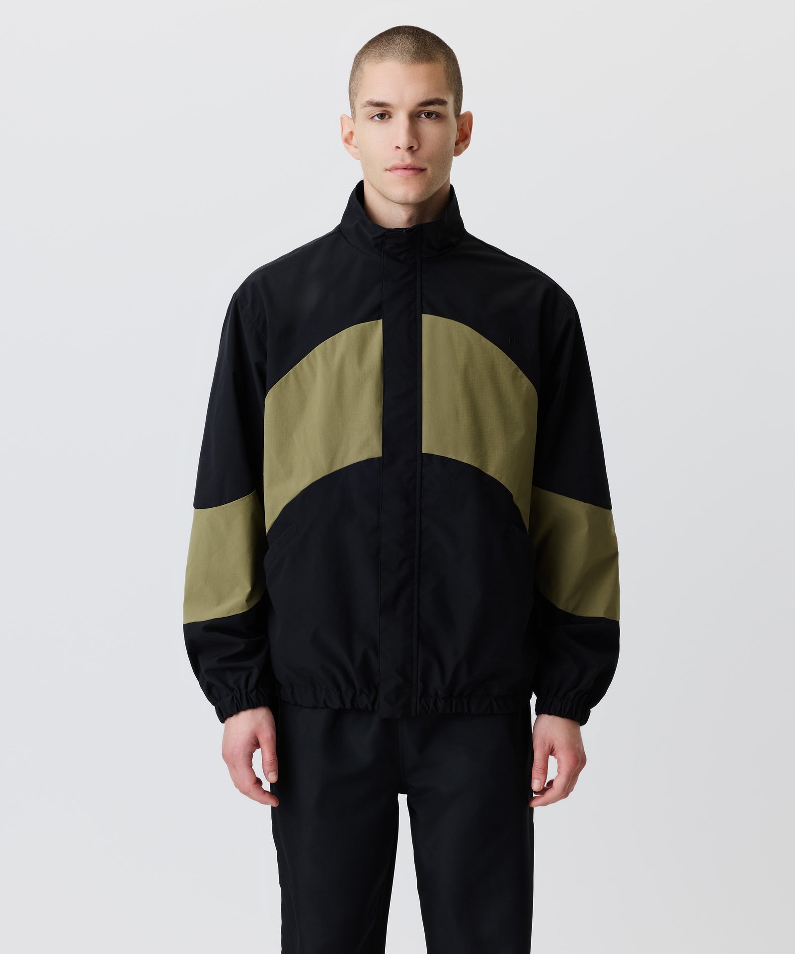 Auf dem Bild in der Front-Ansicht trägt der Mann den Wind-Breaker in Kombination mit einer schwarzen Hose. 