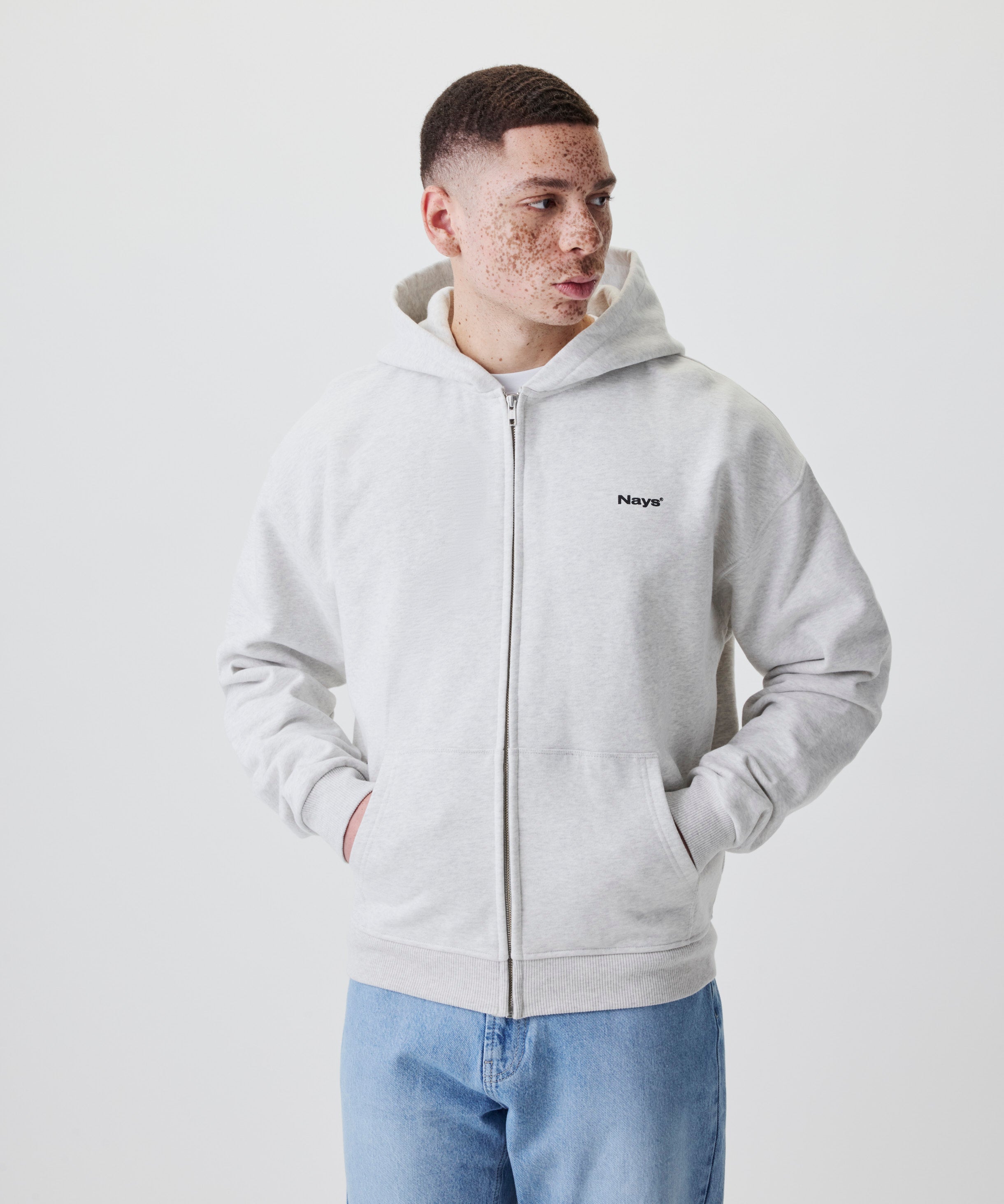 Hellgrauer Zip-Hoodie mit Nays-Logo und Kapuze in der Seitenansicht, kombiniert mit blauer Jeans.
