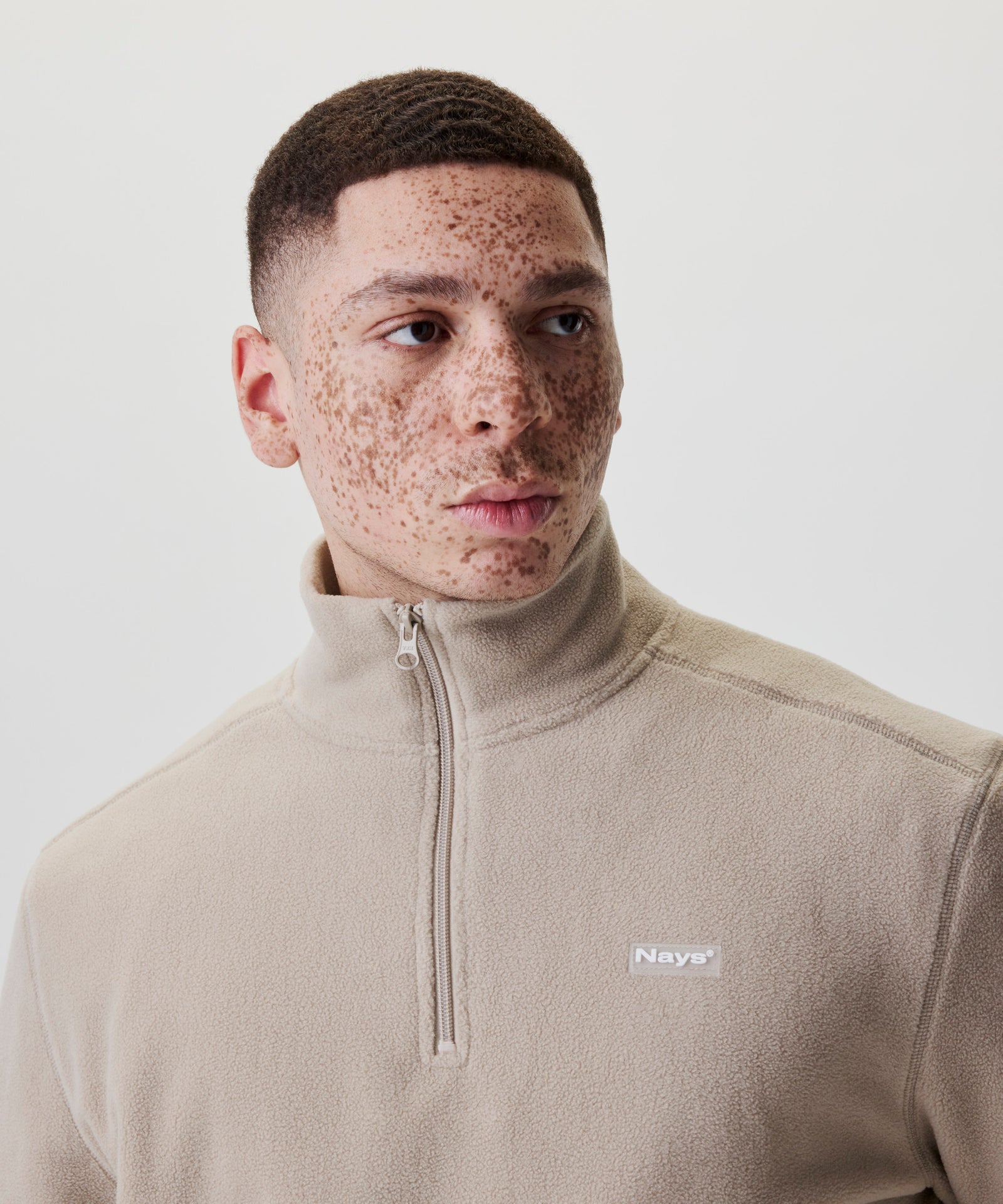 Nahaufnahme beiger Fleece-Troyer mit Nays Logo-Patch.