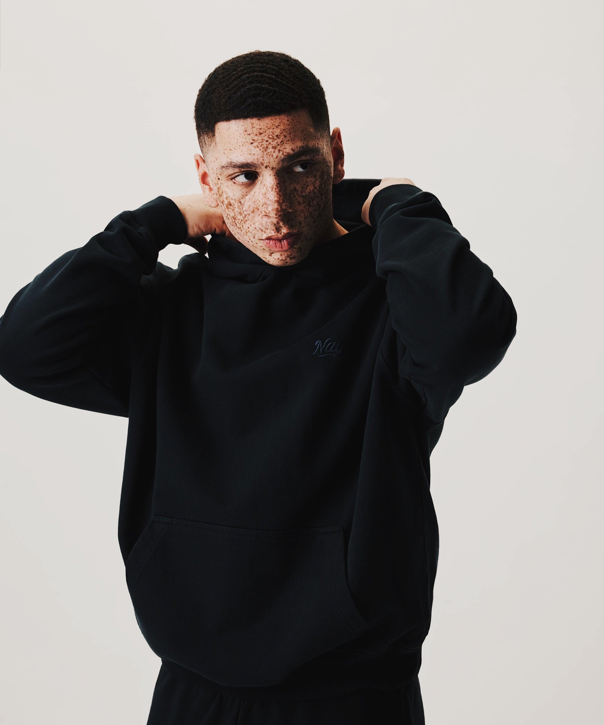 Model in schwarzem NAYS new Script Hoodie vor cleanem Studiohintergrund mit Fokus auf minimalistisches Design und relaxed Fit.