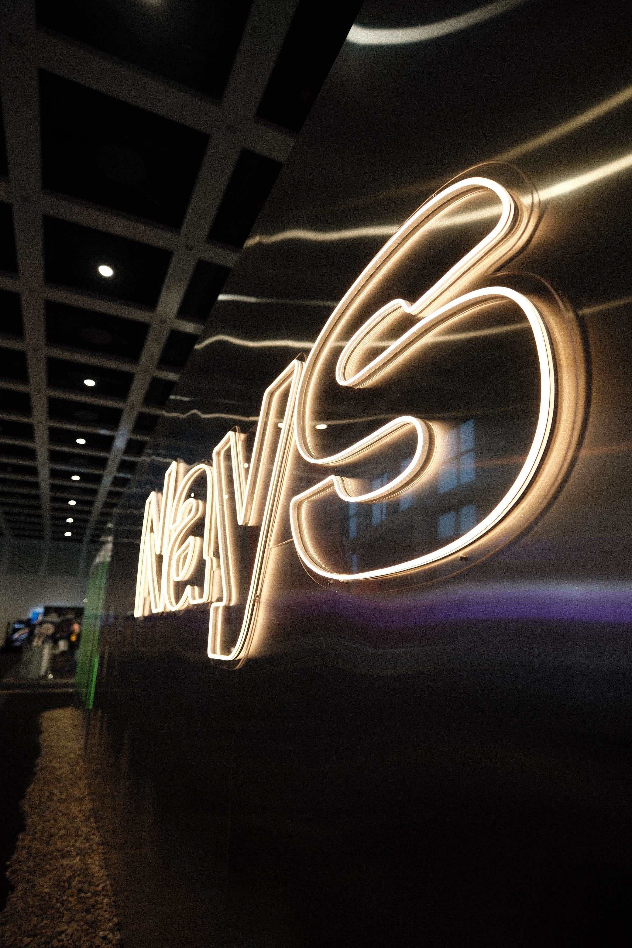 Gold-leuchtender NAYS Neon-Schriftzug auf moderner Aluminium Wand.