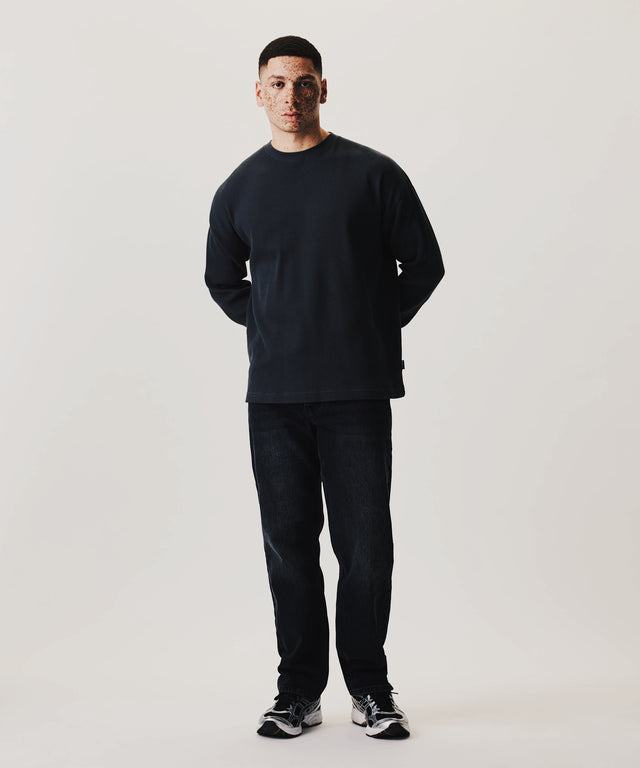 Model in Waffle Longsleeve und dunkler Denim vor cleanem Studiohintergrund mit minimalistischer Silhouette und relaxed Fit.