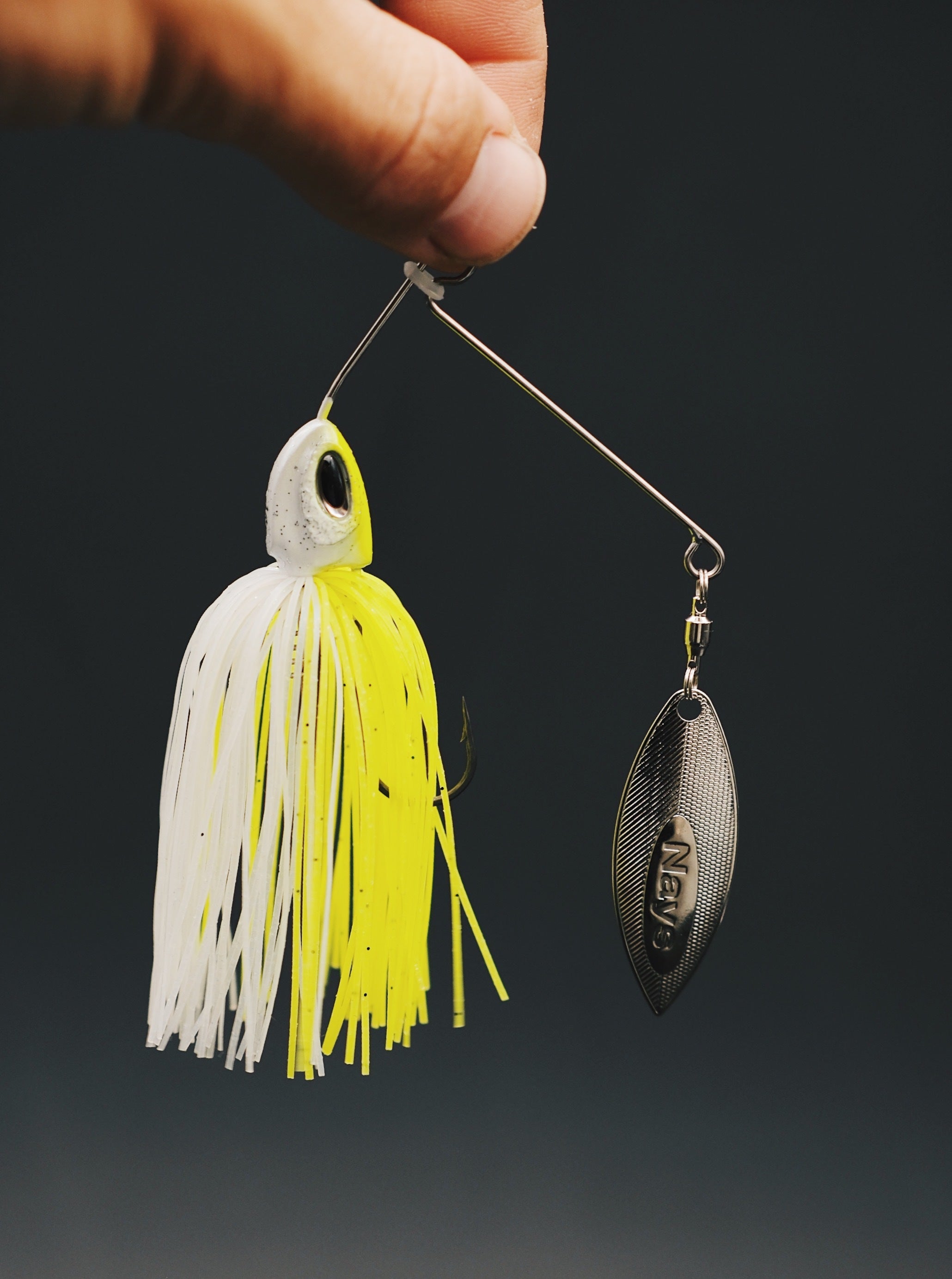 Nays Spinnerbait Raubfischköder in Chartreuse-Weiß mit einem silbernen Willow-Spinnerblatt gehalten von einer Hand vor dunklem Hintergrund.