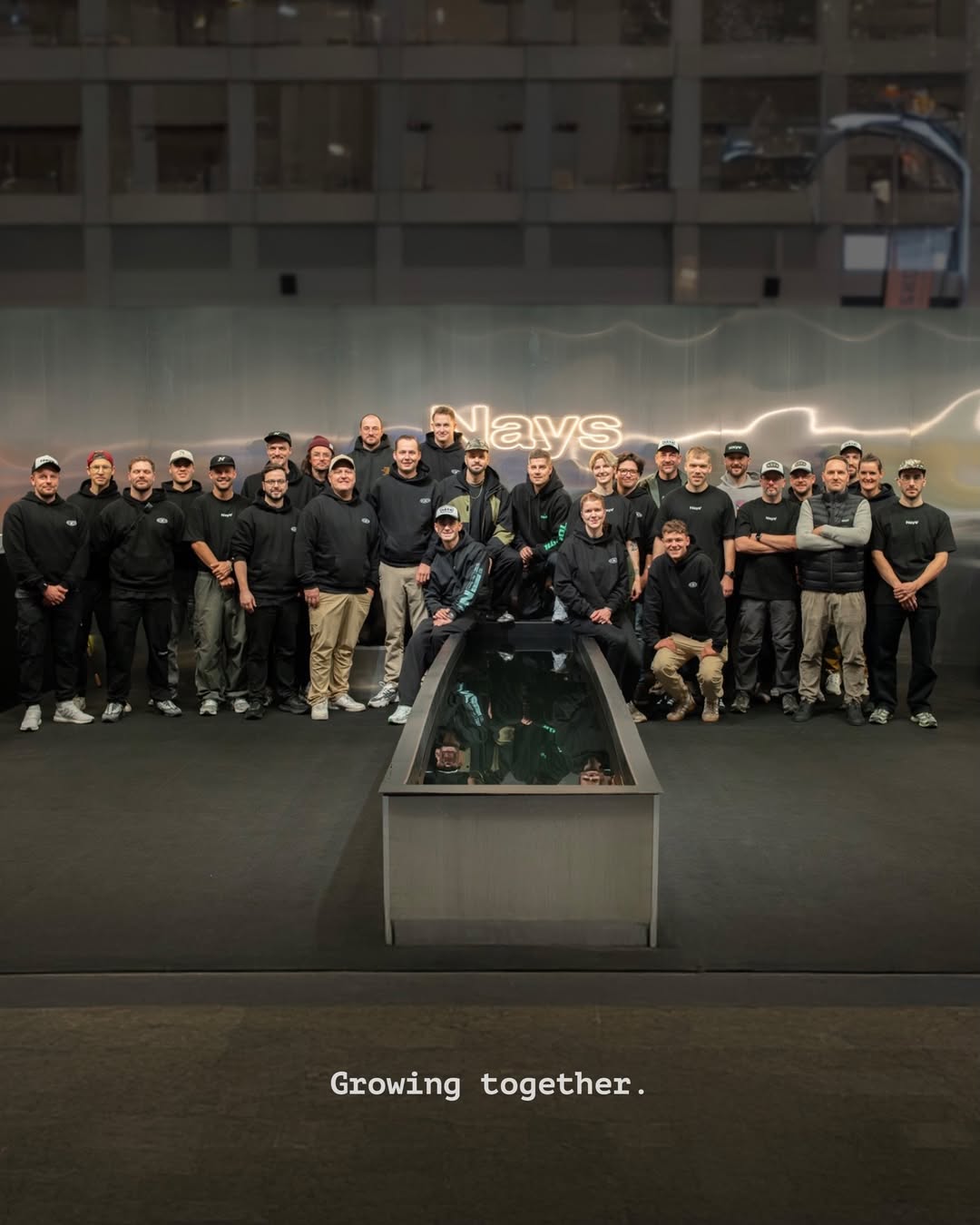 Gruppenfoto des Nays Teams zum 7-jährigen Jubiläum vor dem Nays Logo. Mitarbeiter und Teammitglieder versammelt unter dem Motto „Growing together“.