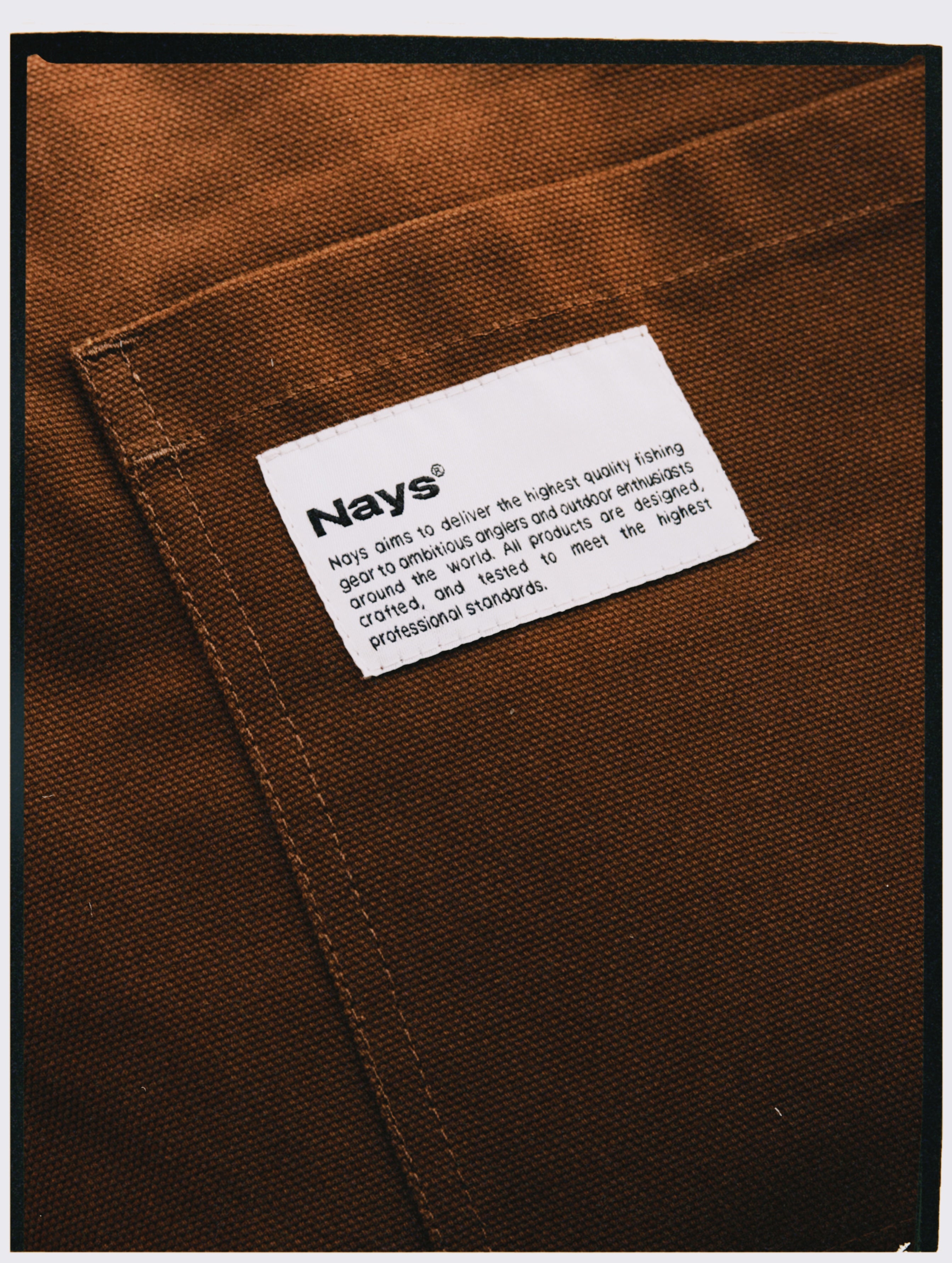 Detailaufnahme NAYS Wovenlabel  auf braunem Canvas mit sichtbaren Nähten.
