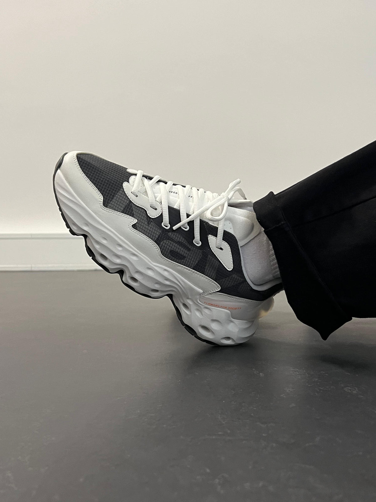 Nahaufnahme des Flowers For Society Seed.One Nays Sneakers getragen am Fuß, Teil einer limitierten Kollaboration, die innovative Designs und einzigartige Silhouetten präsentiert.