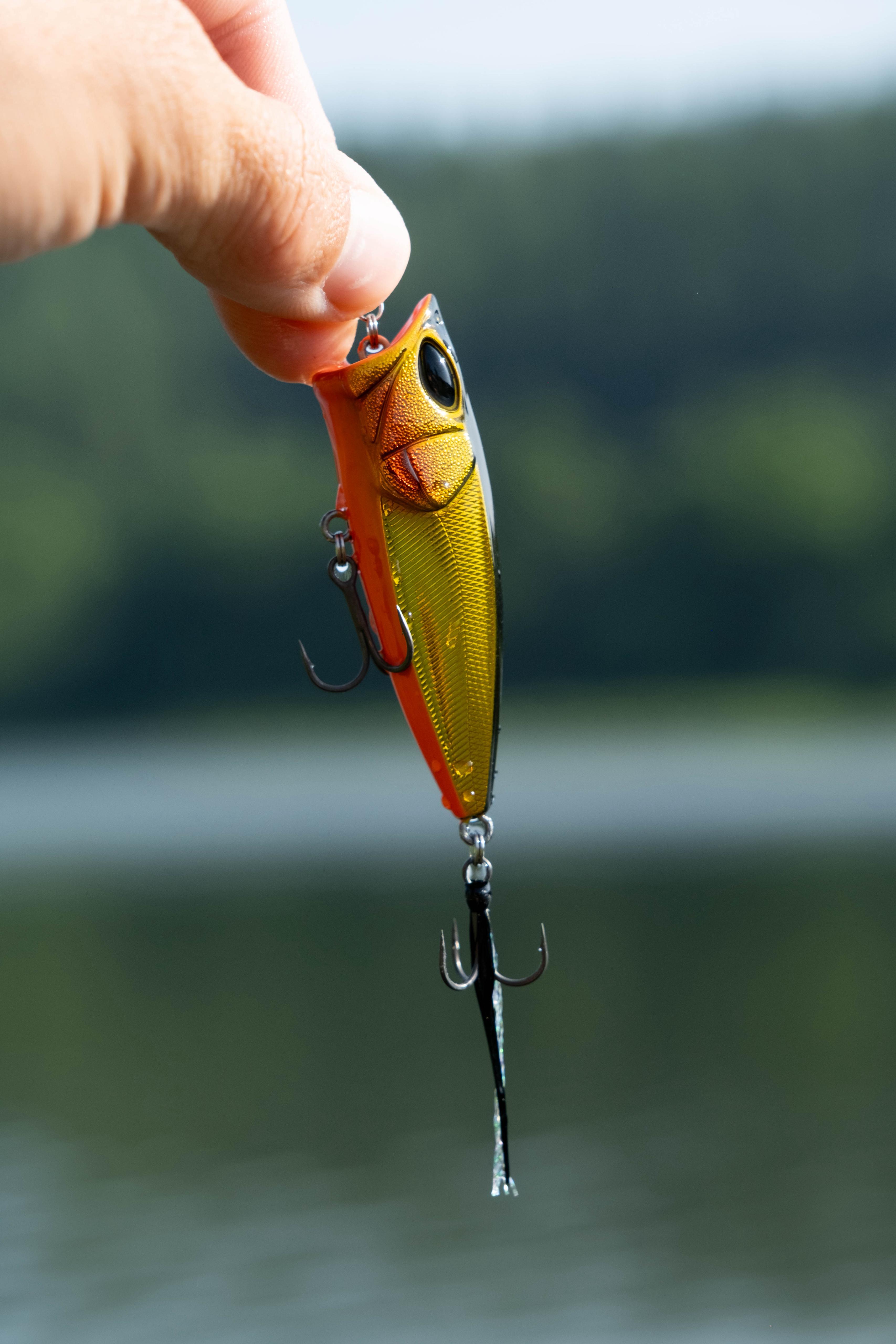 Gold-oranger Popper Angelköder für die Oberflächenangelei auf Barsch und Hecht, nah aufgenommen vor einem Gewässerhintergrund.