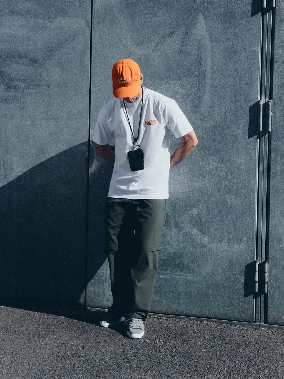 Model in weißem NAYS College Print T-Shirt vor moderner Betonarchitektur mit urbanem Lifestyle-Fokus.