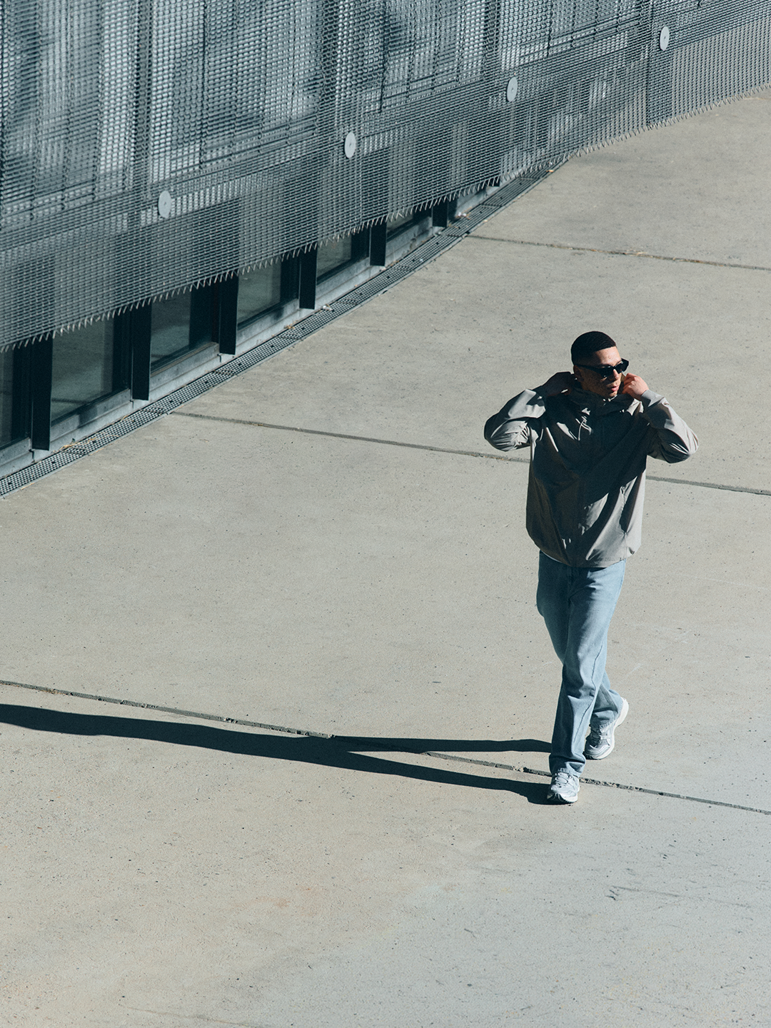 Model in heller 2L Defend Mono NAYS Jacke vor minimalistischer Betonarchitektur im urbanen Setting des Velodrom Berlin.