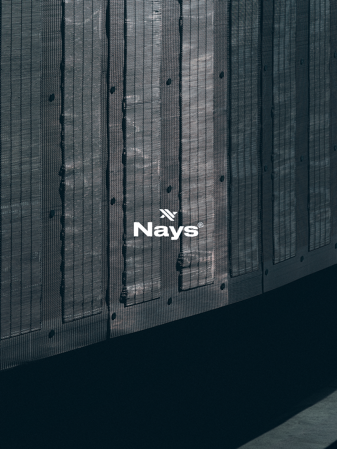 NAYS Logo auf strukturierter Metalloberfläche mit industrieller Architektur und dunklen Schatten.