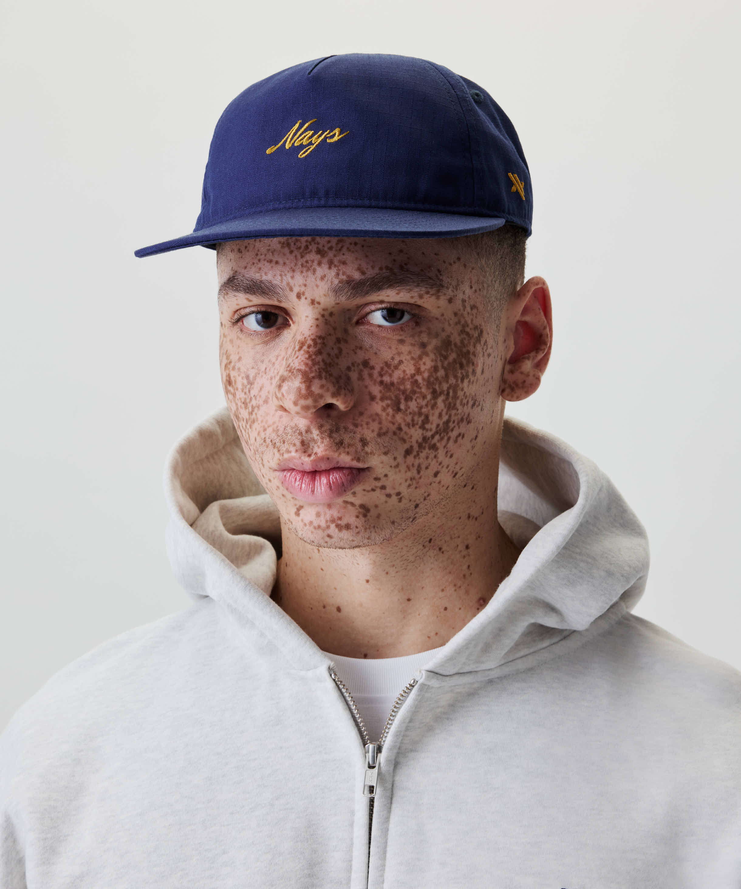 Nahaufnahme eines jungen Mannes mit Sommersprossen, der eine Ripstop Script Cap trägt. Die Kappe hat ein gesticktes gelbes Logo auf der Vorderseite.