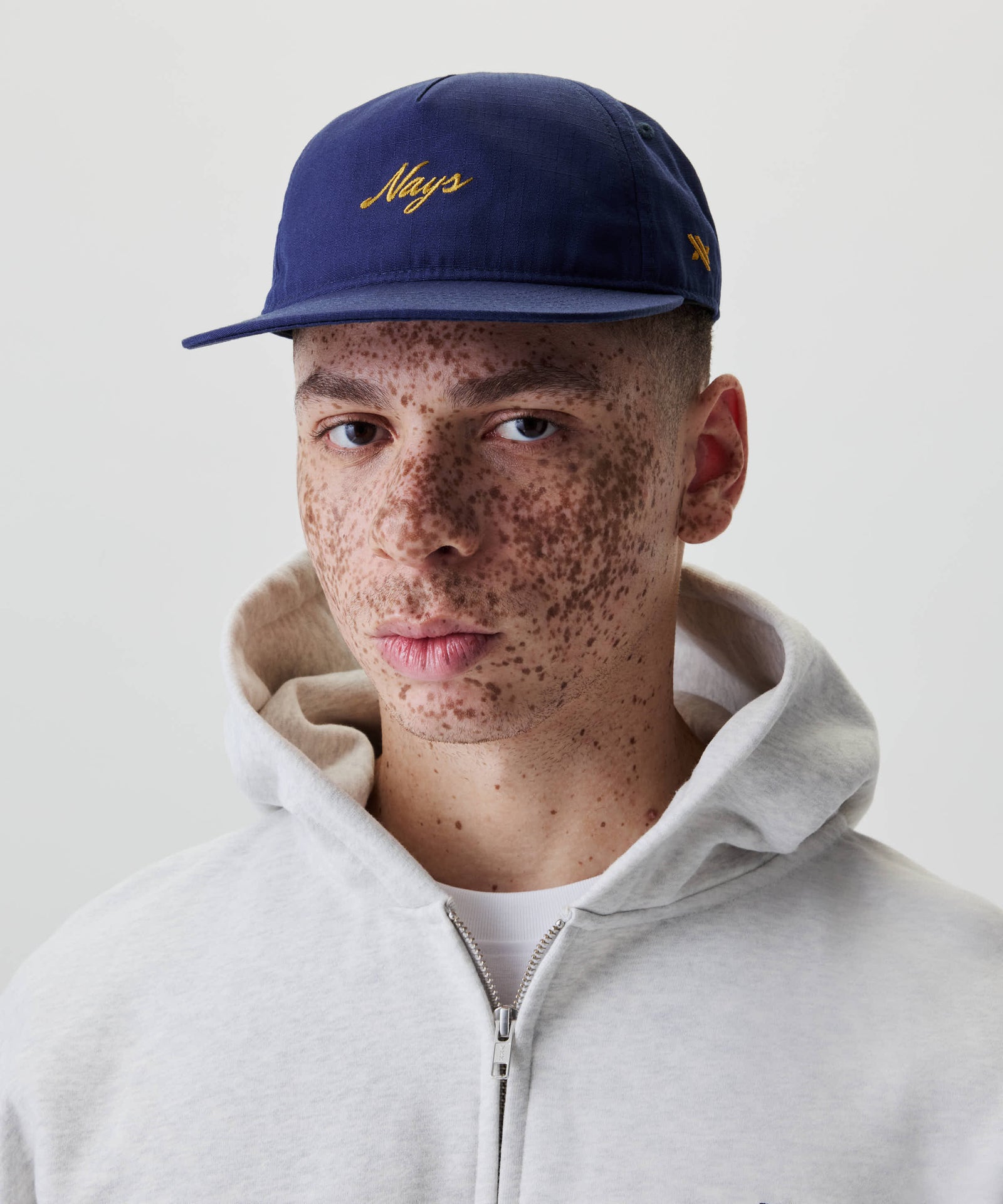 Nahaufnahme eines jungen Mannes mit Sommersprossen, der eine Ripstop Script Cap trägt. Die Kappe hat ein gesticktes gelbes Logo auf der Vorderseite.