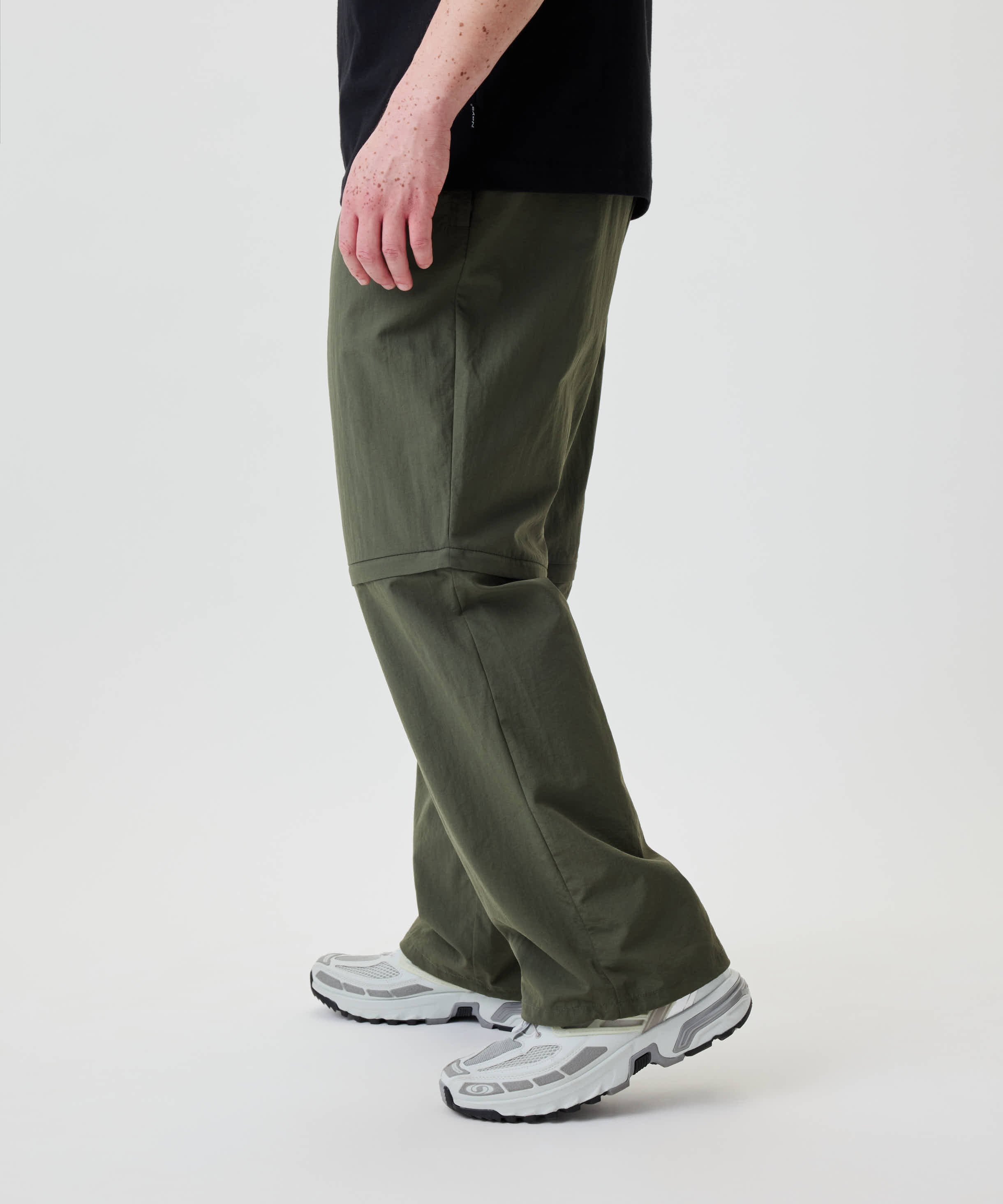 Person trägt Nays Lightweight Zip Off Pants mit abzippbaren Beinen und praktischen Reißverschlusstaschen, kombiniert mit robusten Trail-Sneakers. Ideal für vielseitige Outdoor-Aktivitäten.