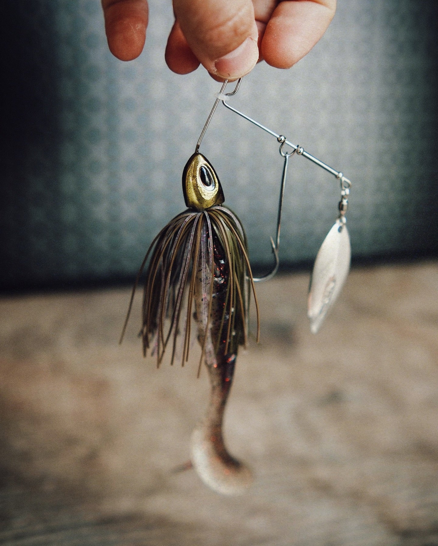 Spinnerbait mit Gummifisch-Trailer, braun-grüner Skirt, silbernes Spinnerblatt, gehaltener Angelköder.