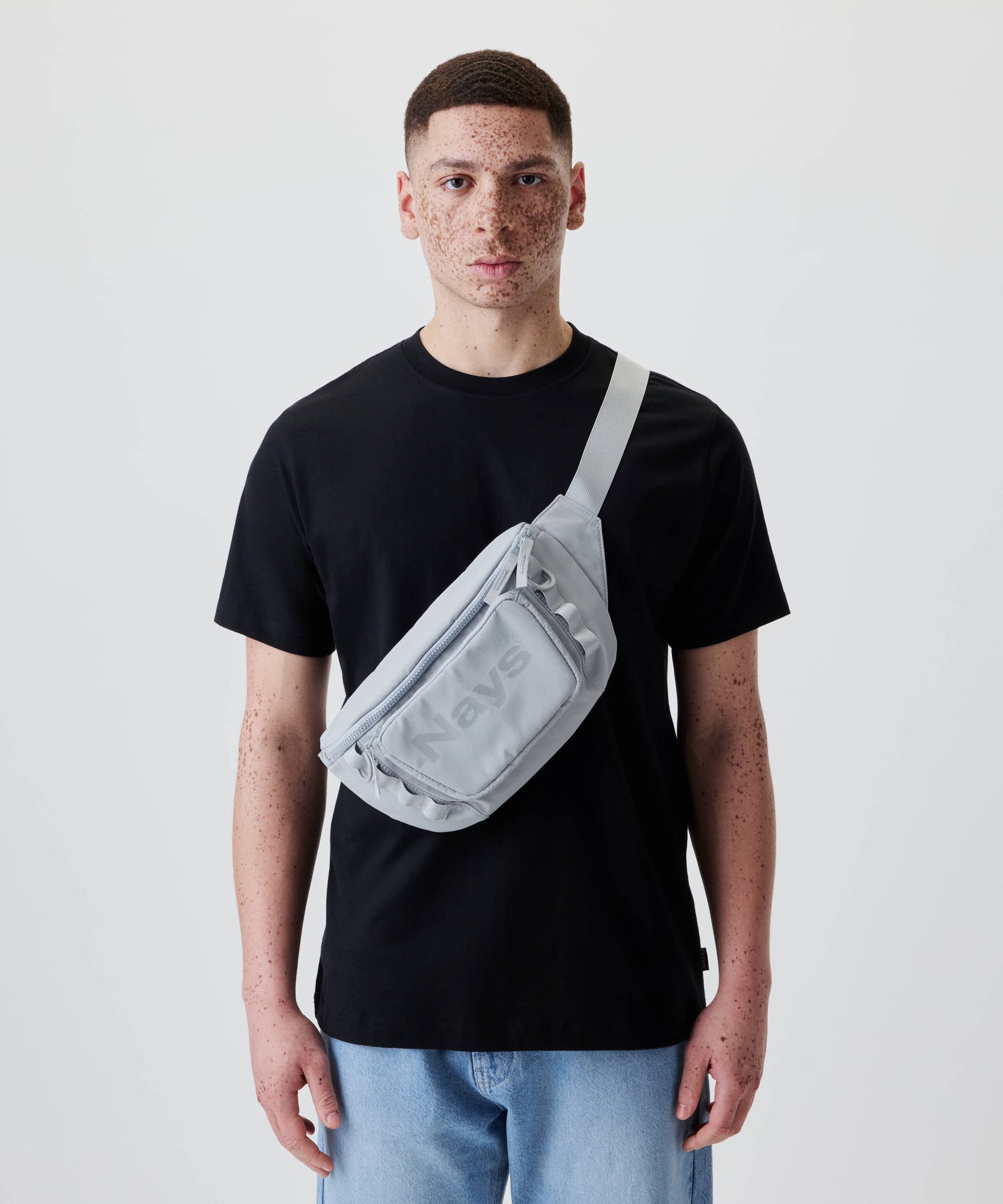 Ein junger Mann trägt die Nays Lightweight Cross Body Bag, eine leichte graue Umhängetasche mit Reißverschluss, ideal für organisierte und flexible Nutzung unterwegs.