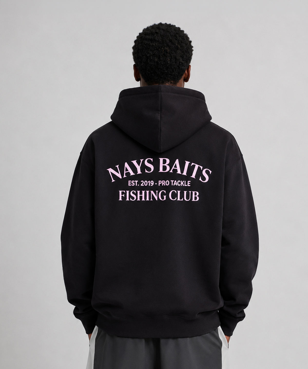 Model trägt Nays Baits Fishing Club Hoodie in Schwarz – Detailansicht der Rückseite mit rosa Logo-Print.