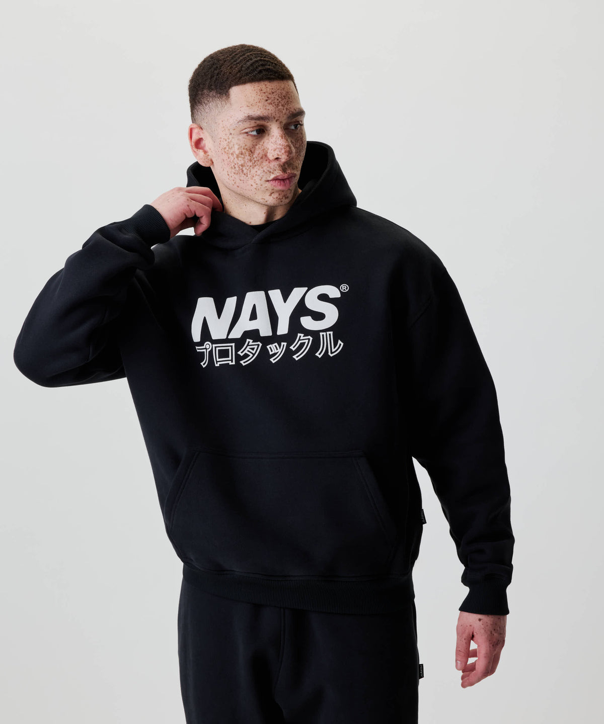 Ein junger Mann trägt den Nays Understatement Hoodie mit weißem Frontprint NAYS und Katakana-Zeichen, präsentiert im lässigen, oversized Stil.