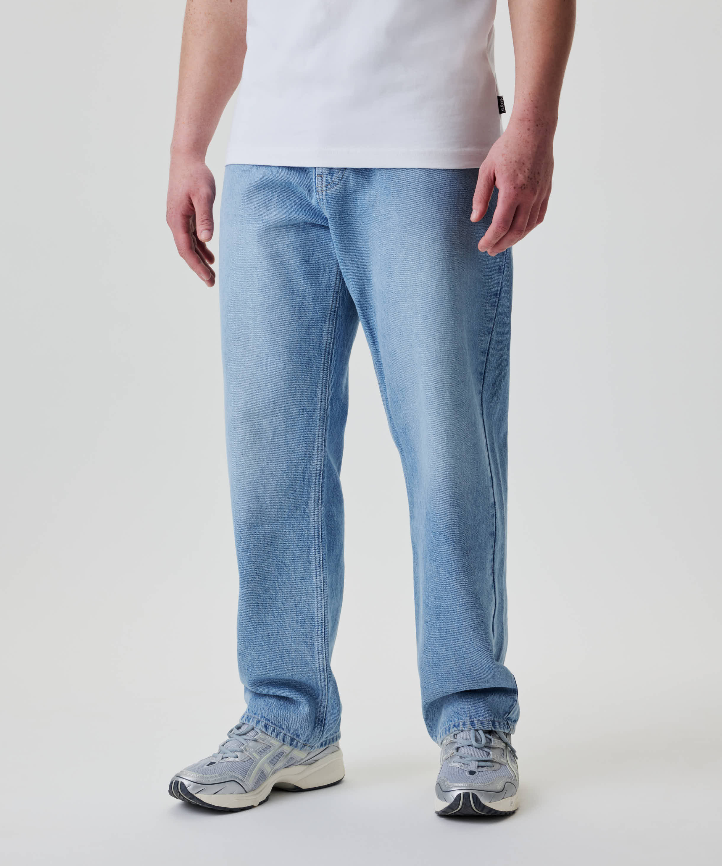 Person trägt Nays Straight Fit Jeans, hell gewaschen, aus 100% Baumwoll-Denim, mit klassischem 5-Pocket-Design, kombiniert mit grauen/weißen Sneakers und weißem T-Shirt.