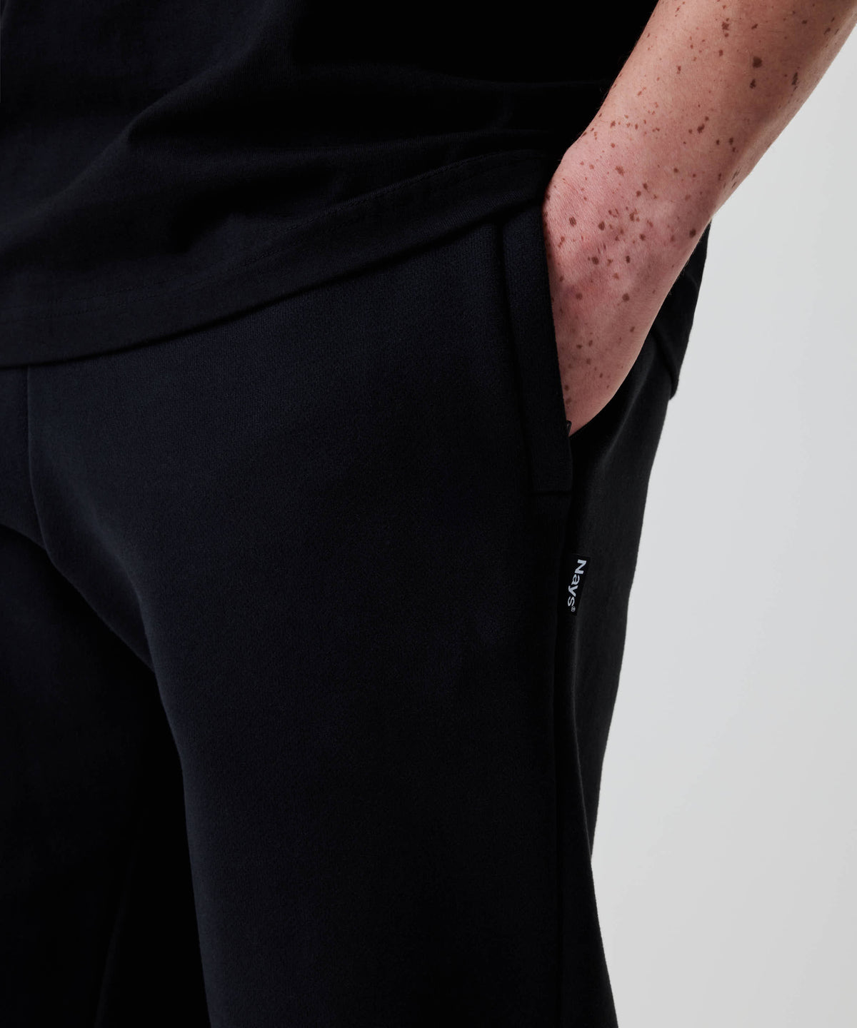Eine freihändige Nahaufnahme zeigt Nays Classic Sweatpants in Schwarz mit Regular Fit, kleinem Label an der Seitennaht und handlicher Tasche.