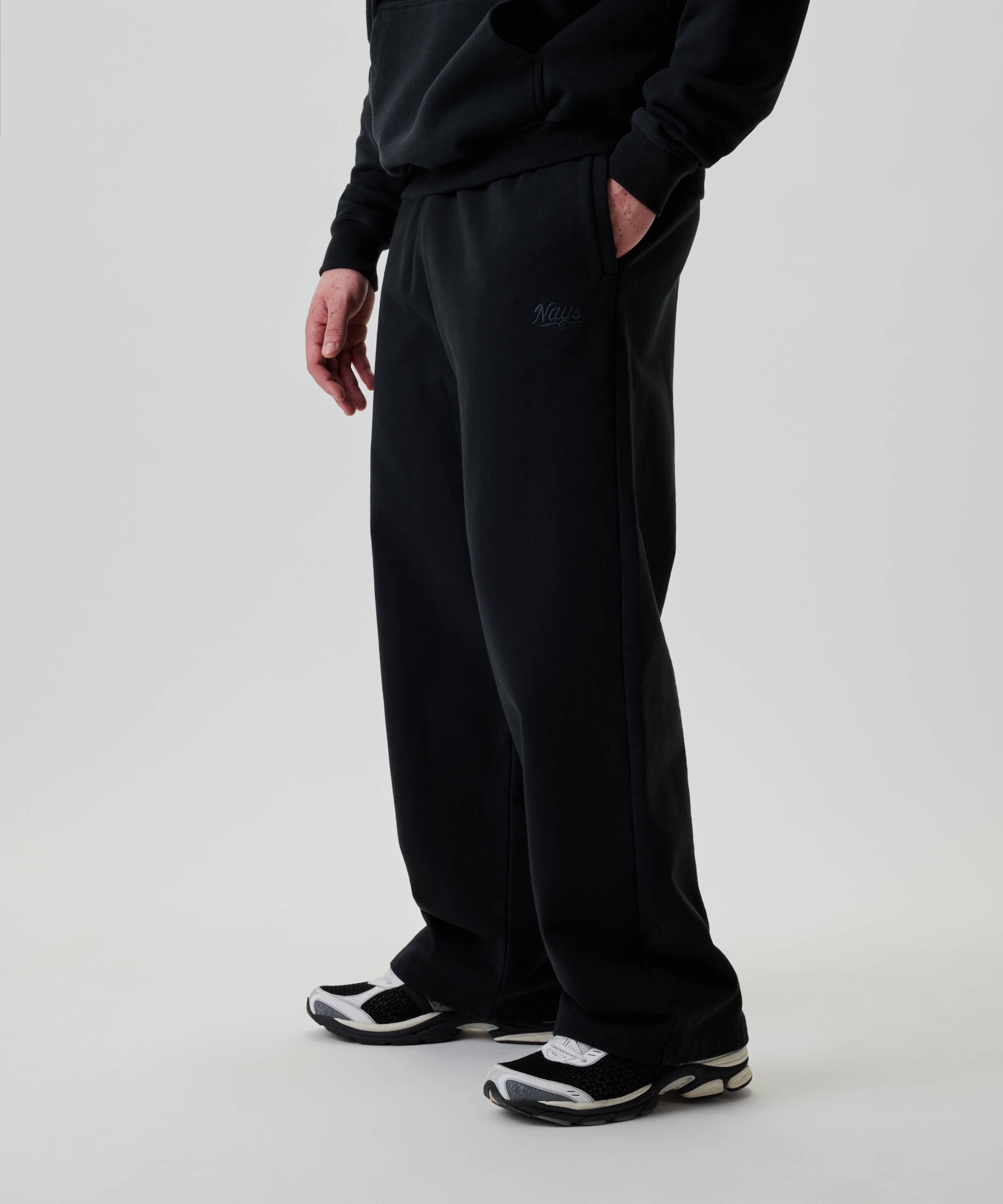 Modell trägt Nays Straight Leg Sweatpants, locker geschnitten, mit kleinem Logo auf der Hüfte. Hände in Taschen, kombiniert mit schwarz-weißen Sneakers.