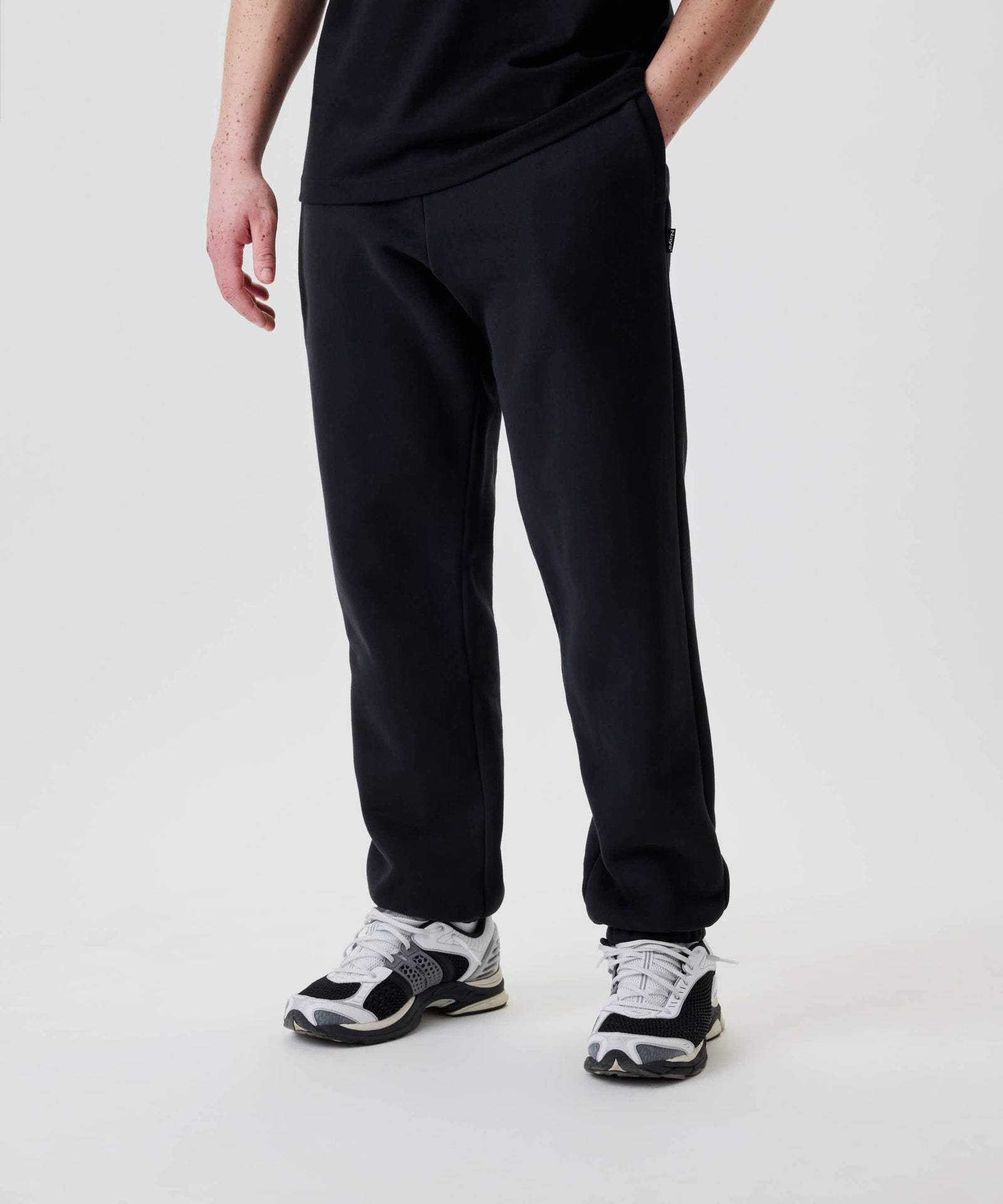 Person trägt Nays Classic Sweatpants, Regular Fit, gebrushte Innenseite, mit YKK Zipper-Taschen. Schwarzes T-Shirt sichtbar, Hände locker an den Seiten.