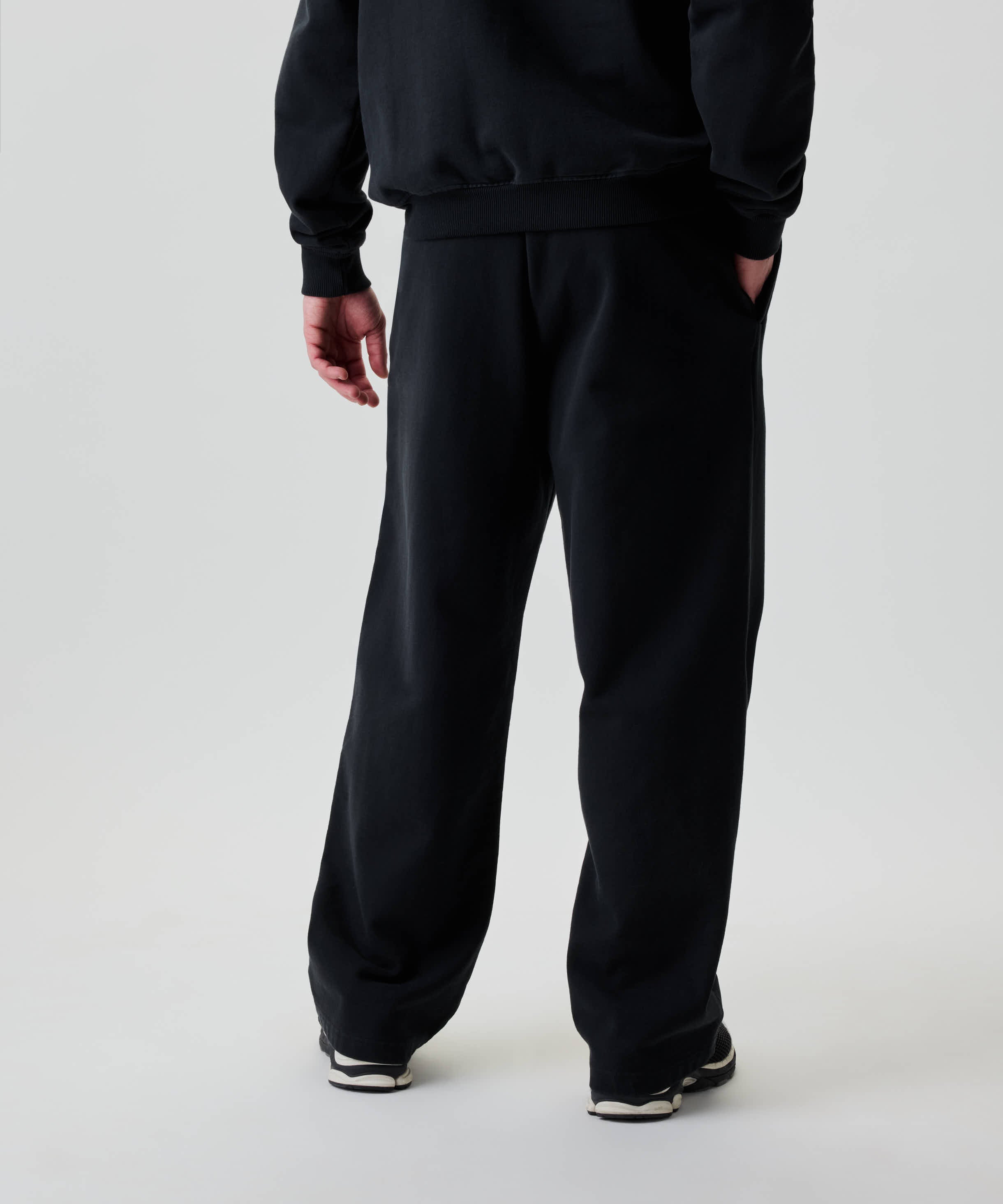 Person von hinten mit Nays Straight Leg Sweatpants, locker geschnitten, Taschen mit YKK Zippern, kombiniert mit schwarz-weißen Sportschuhen.